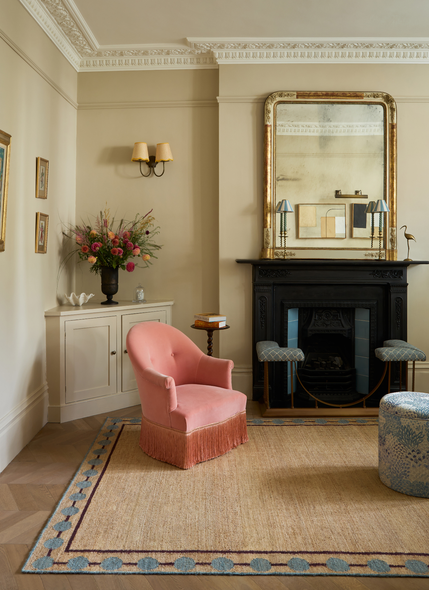 a living room with beige walls, a pink velvet fringed armchair and a large black fireplace