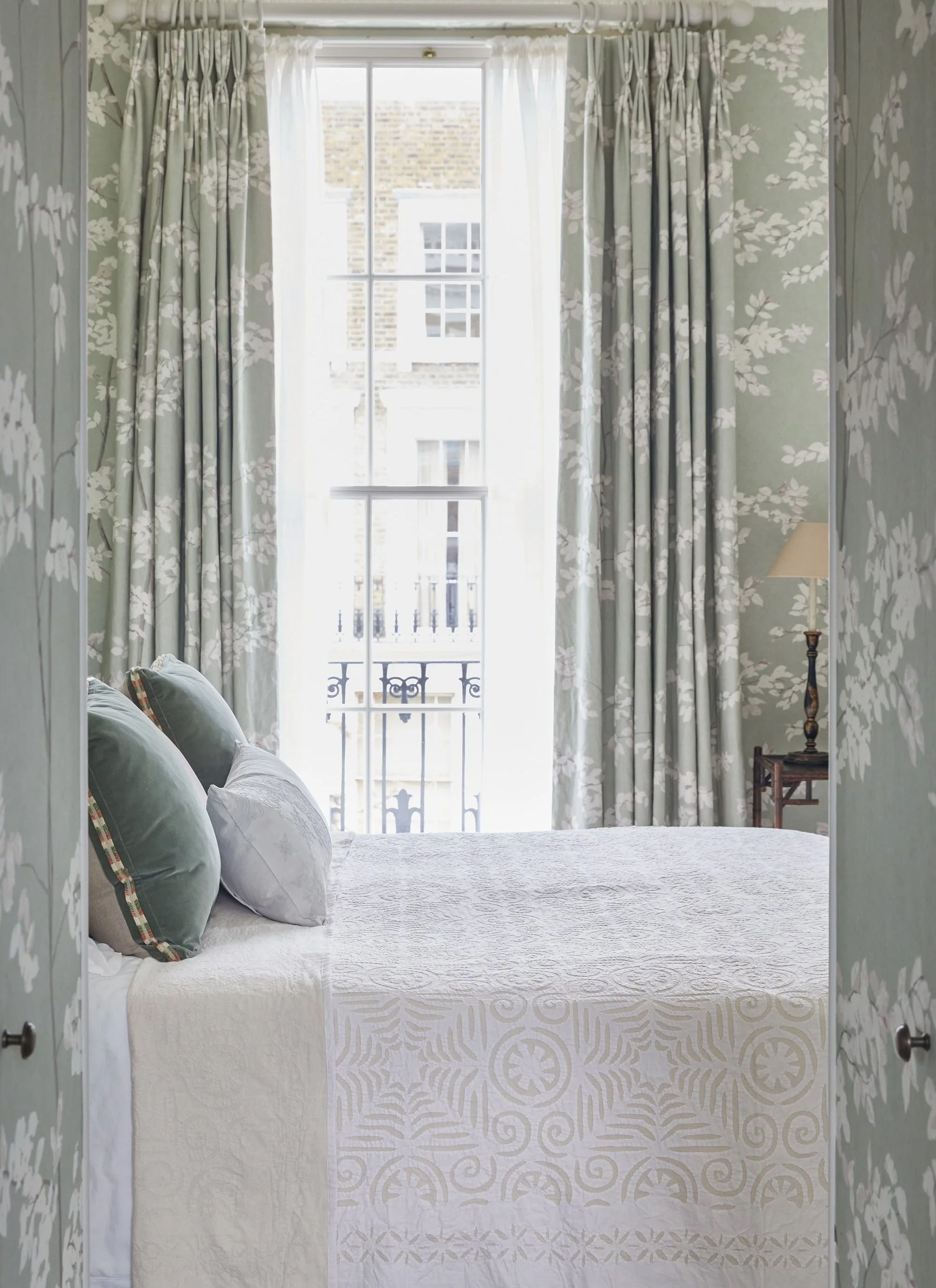 a bedroom with sage green and white leaf pattern wallpaper and amtching curtains and a bed with white bedding