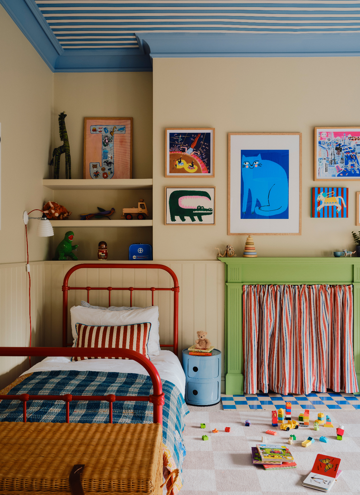 a childrens bedroom with cream walls, a blue and white stripe ceiling, a green fireplace and a red iron bed frame