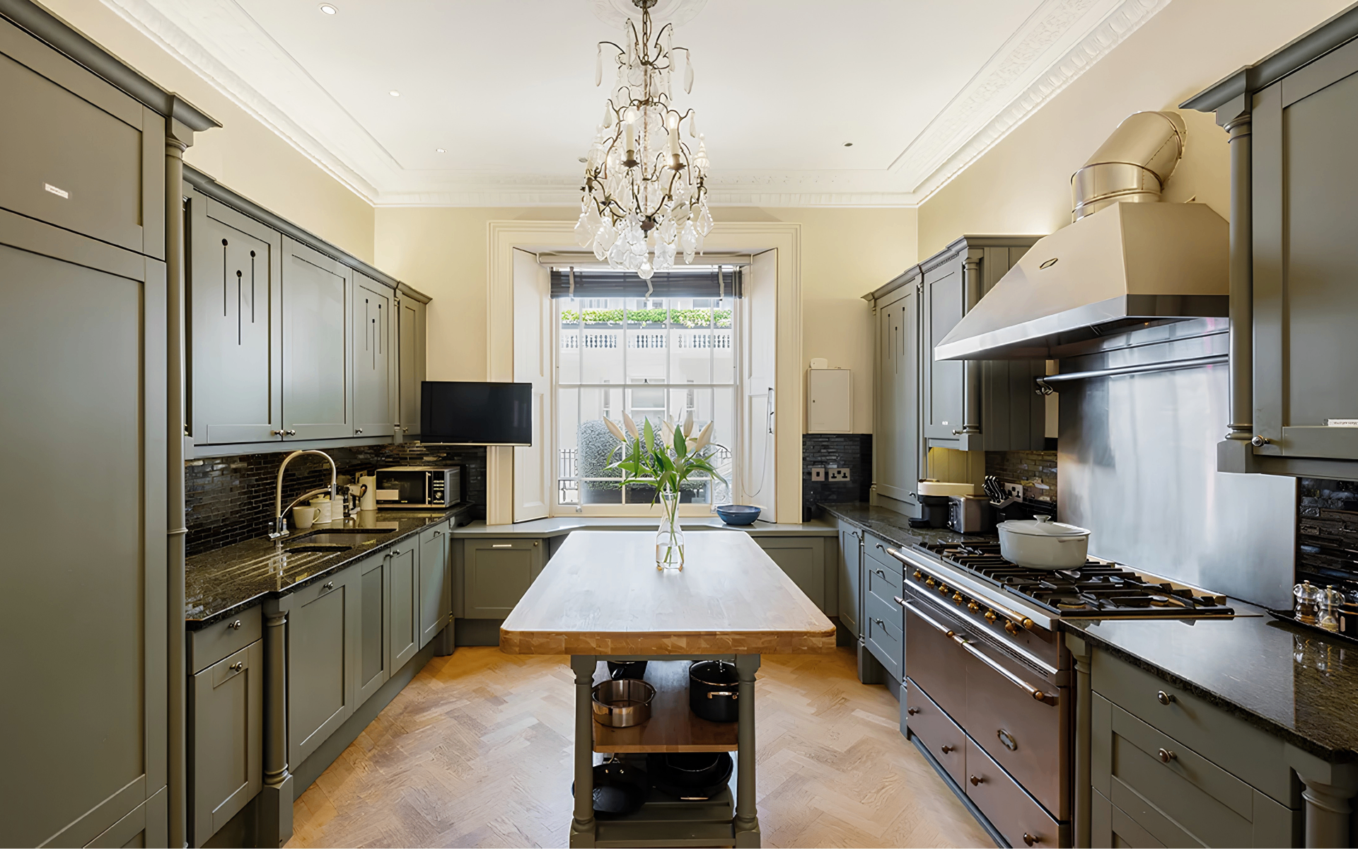 a kitchen with dark olive green cabinetry, a wooden kitchen island and a large chandelier pendant