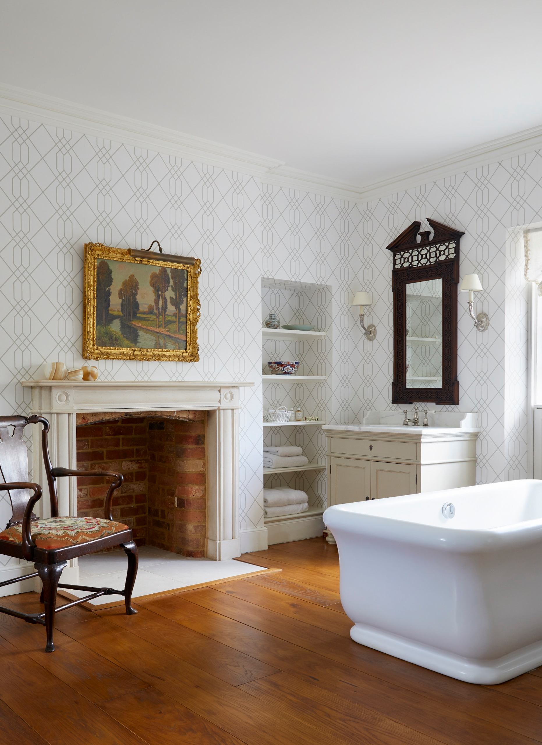a large bathroom with wooden flooring, a large white bathtub and a white fireplace with a lanscape painting in a gold frame above it