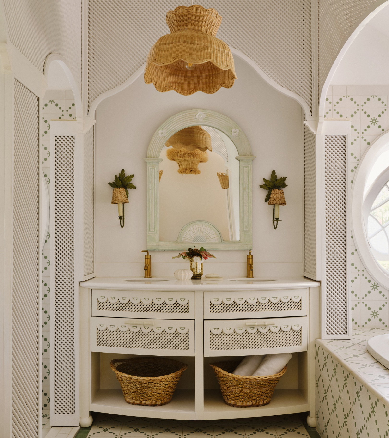 a white ensuite with white and green patterned all over tiles, a wicker pendant and two wicker wall lights beside a mirror