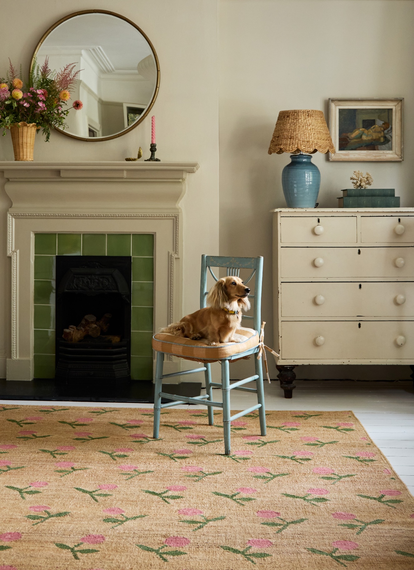 a living room with jute floral rug, a blue wooden chair with a long haired dachsund sat on it and a cream painted fireplace