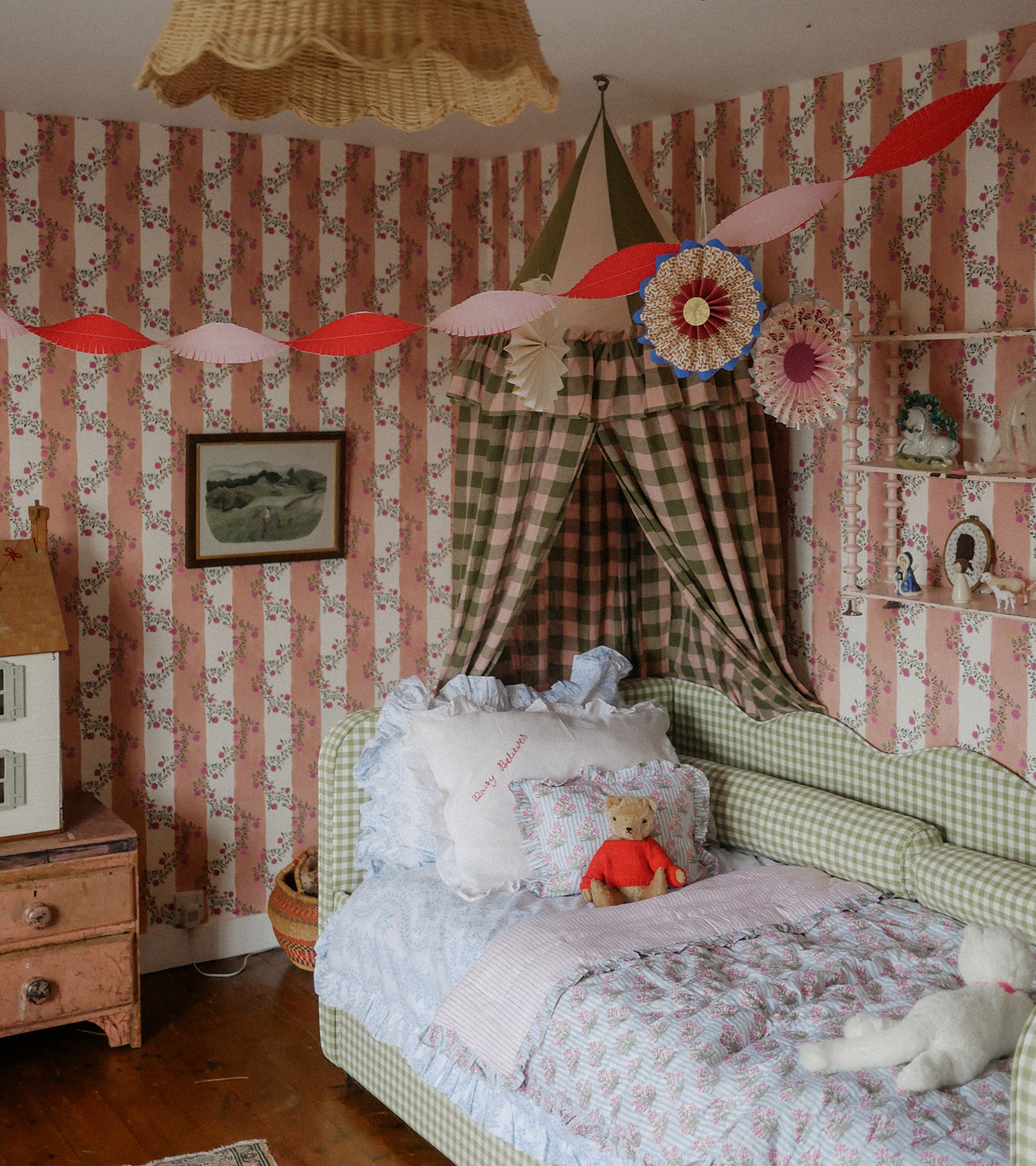 a children's bedroom with pink and white stripe wallpaper, a green gingham daybed with a teddy bear and white bedding and a pink and olive green canopy