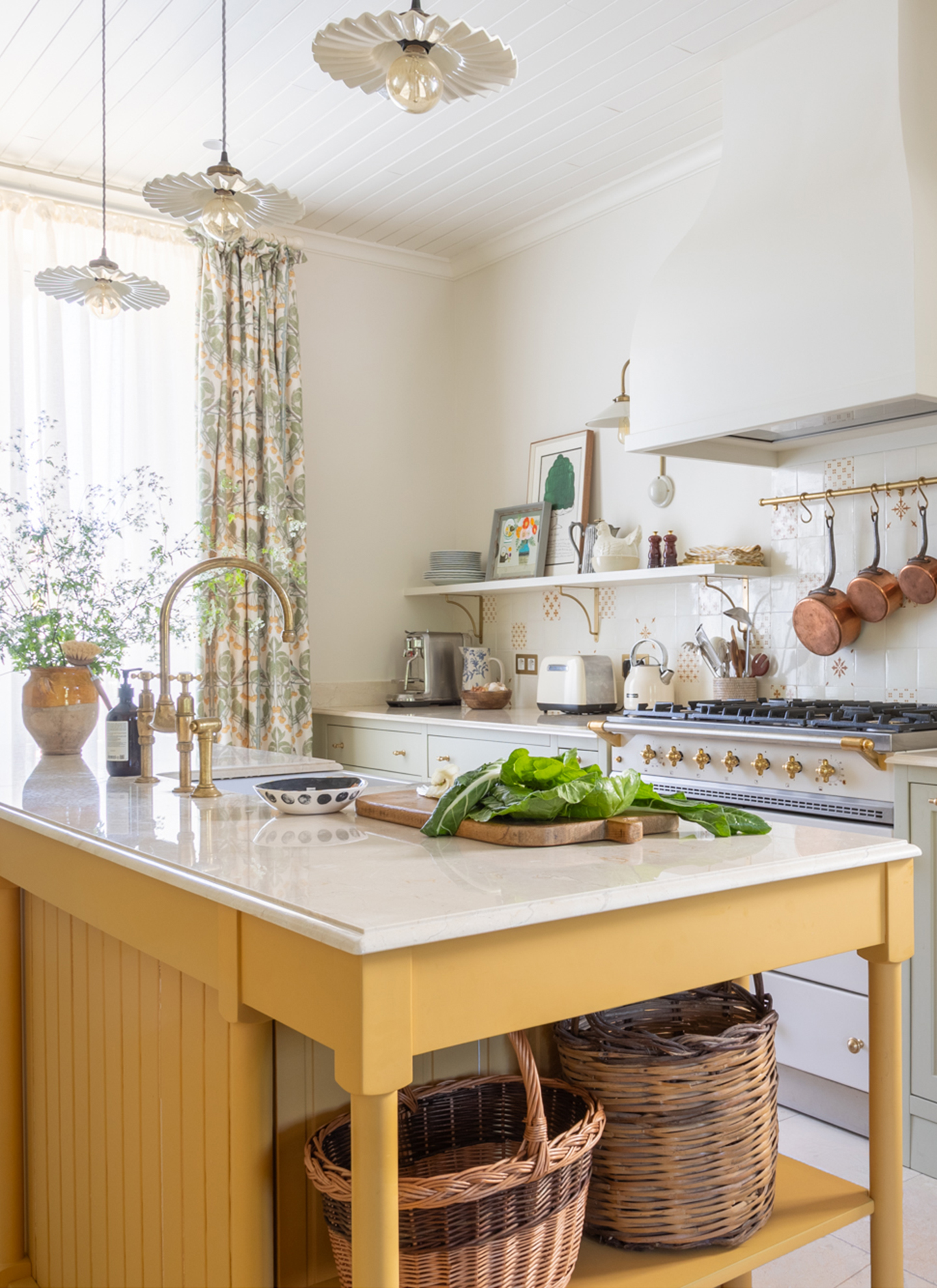 A KITCHEN WITH a yellow freestanding kitchen island and 3 matching scalloped pendants hanging above it