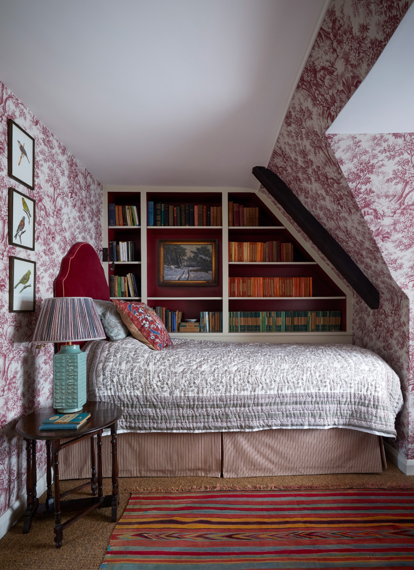 a bedroom with eaves ceiling wrapped in a pink and white toile de jouy wallpaper