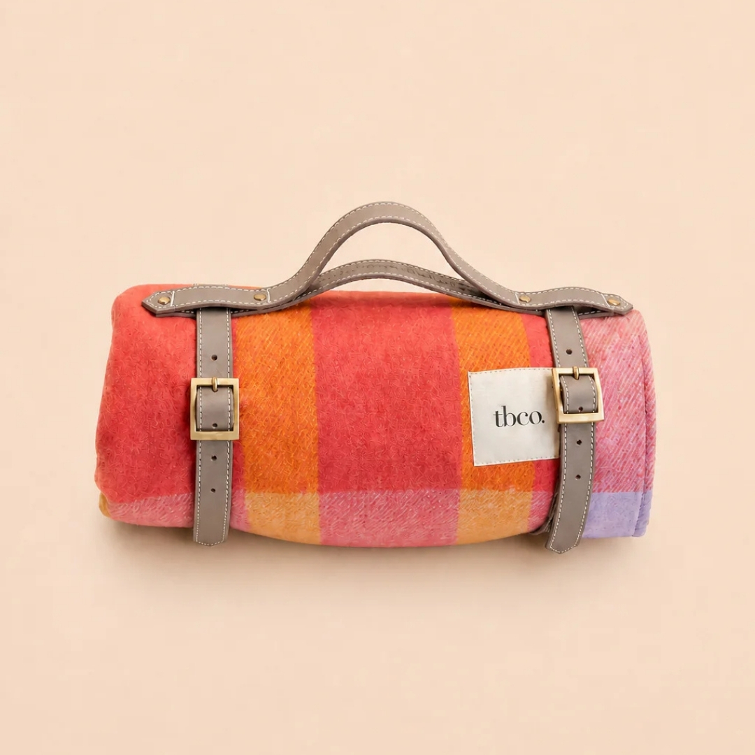 tbco picnic blanket pictured on an orange background in orange and pink colourway