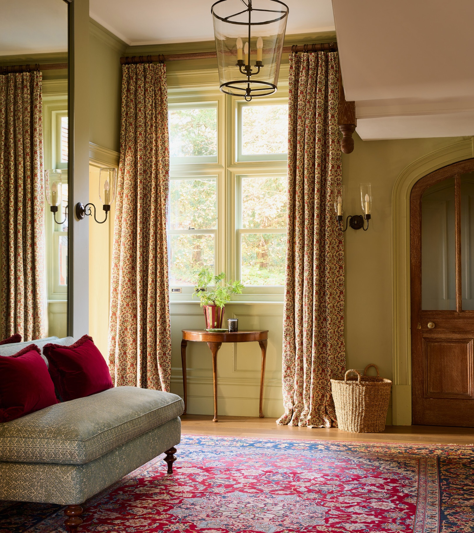 a grand hallway with green and white walls, a red patterned carpet and long neutral floral curtains