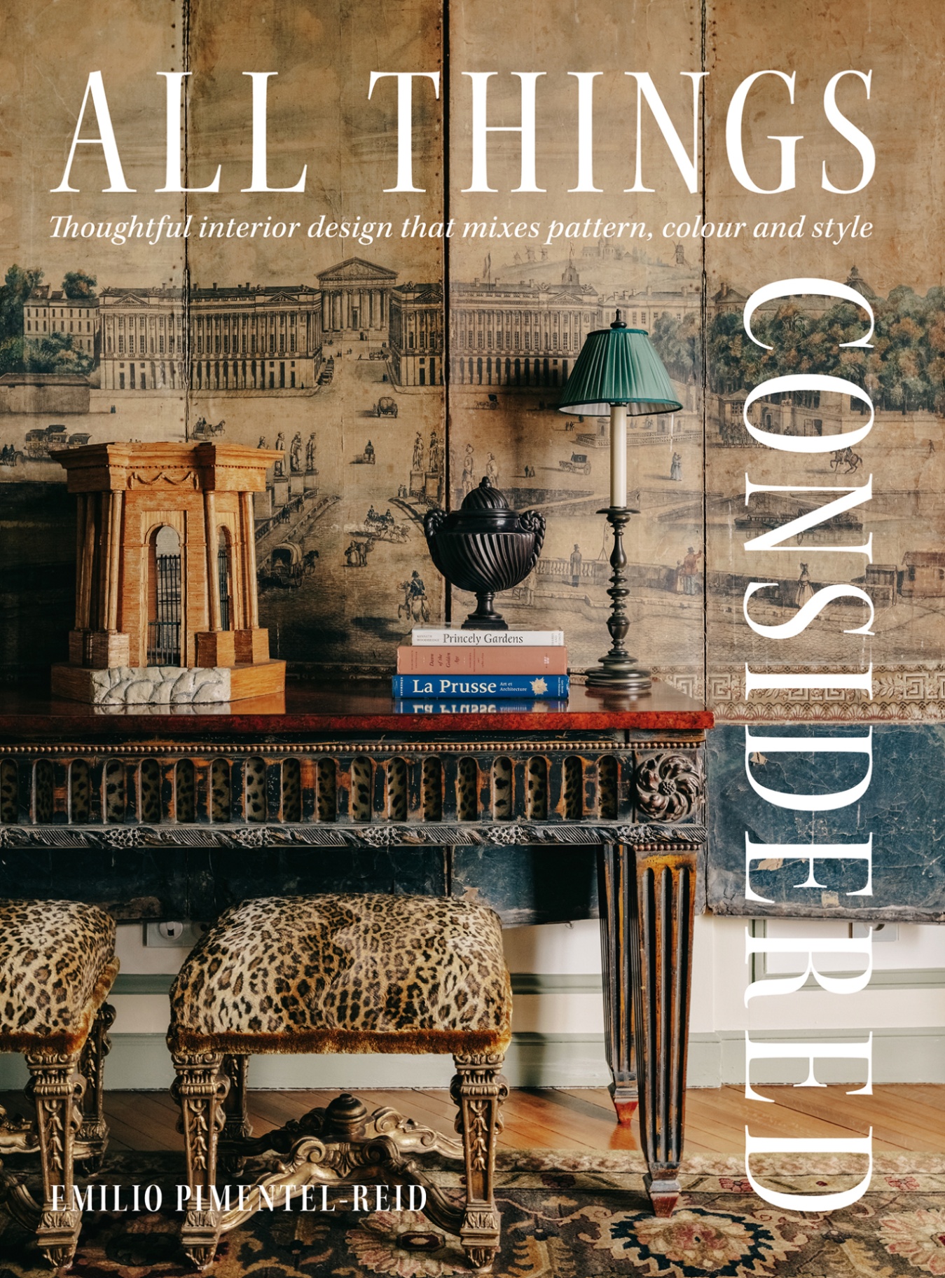 the front cover of the book All Things Considered showing a close up of animal-print stools and a console table topped with books, objects and a lamp, in front of a mural wall