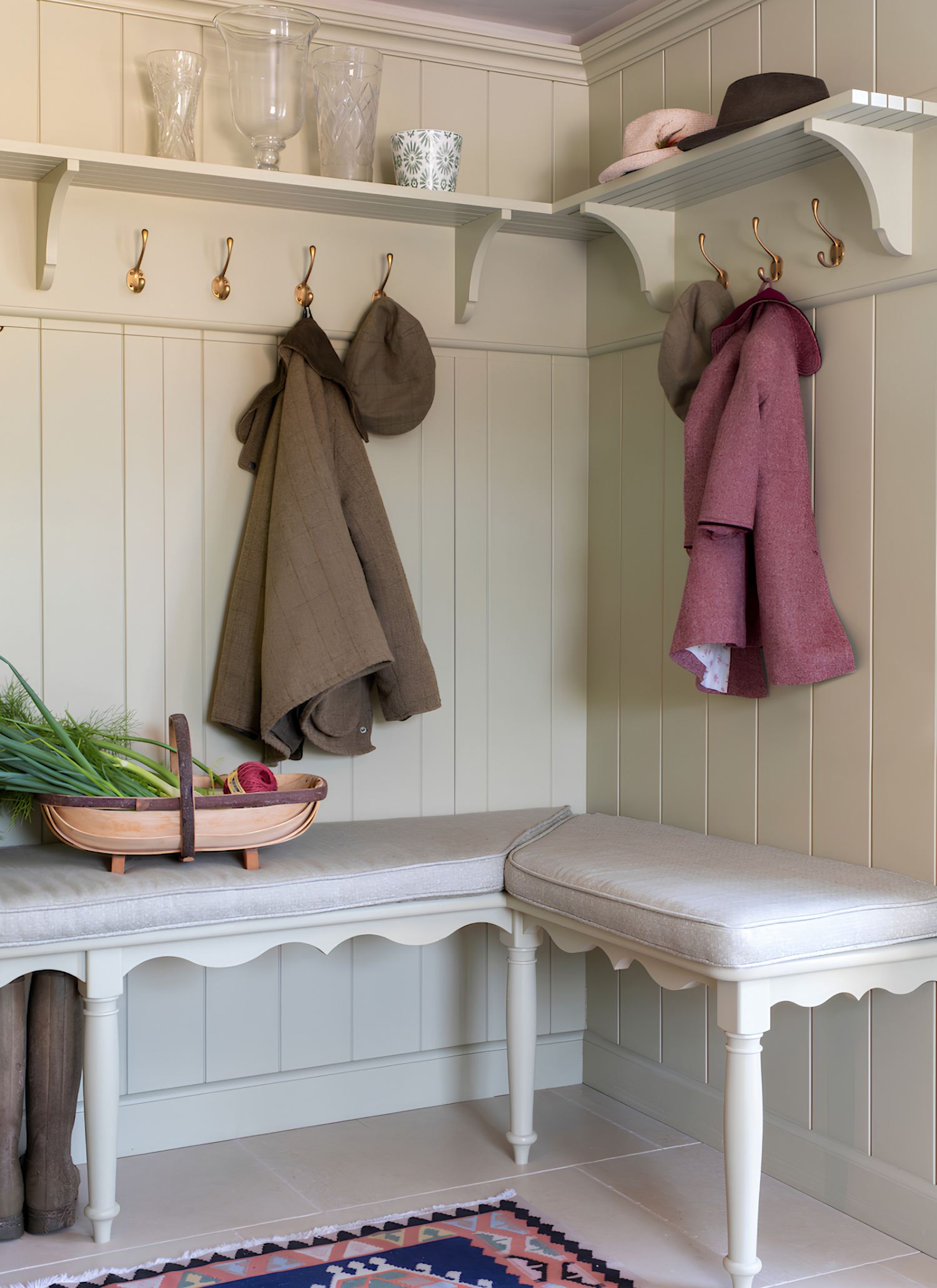 a boot room corner with very pale green paneled walls, a corner bench and shelves with hooks and coats hanging