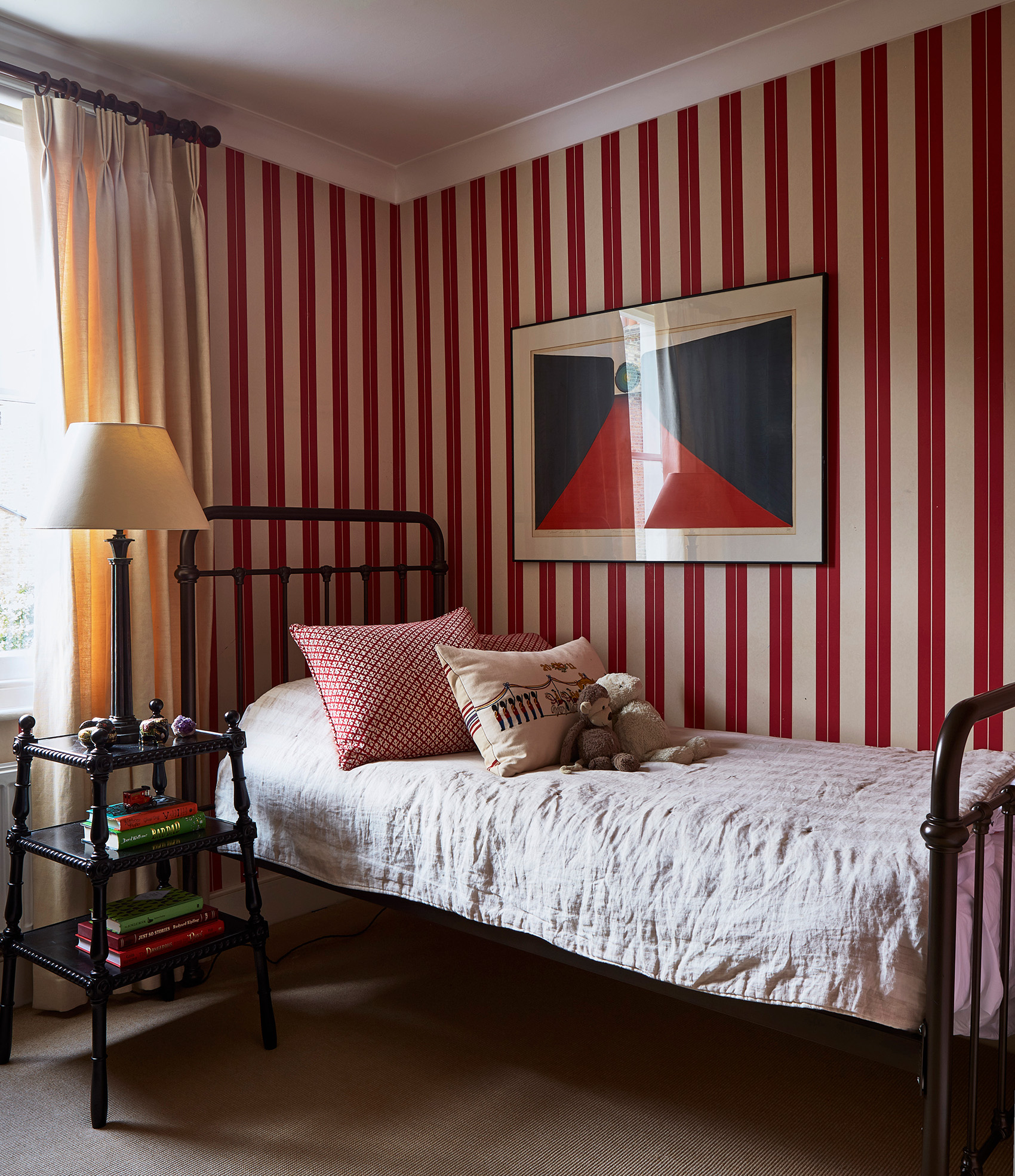 a childrens bedroom with white and red striped wallpaper, a black iron bed with white bedding and a black bedside table with a large lamp