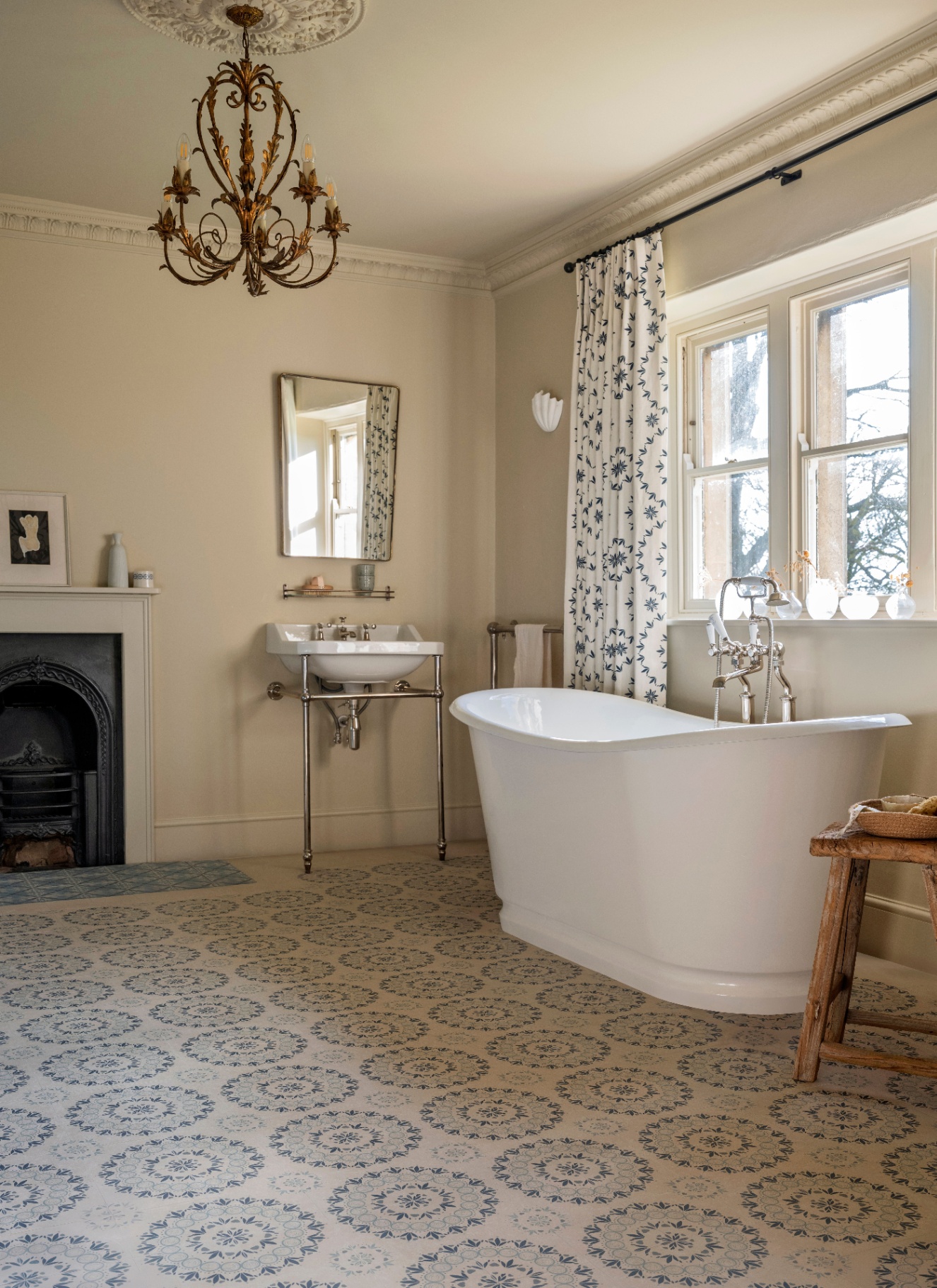 a bathroom with a chandelier and cornicing, a blue and white patterned floor and a large freestanding bath tub