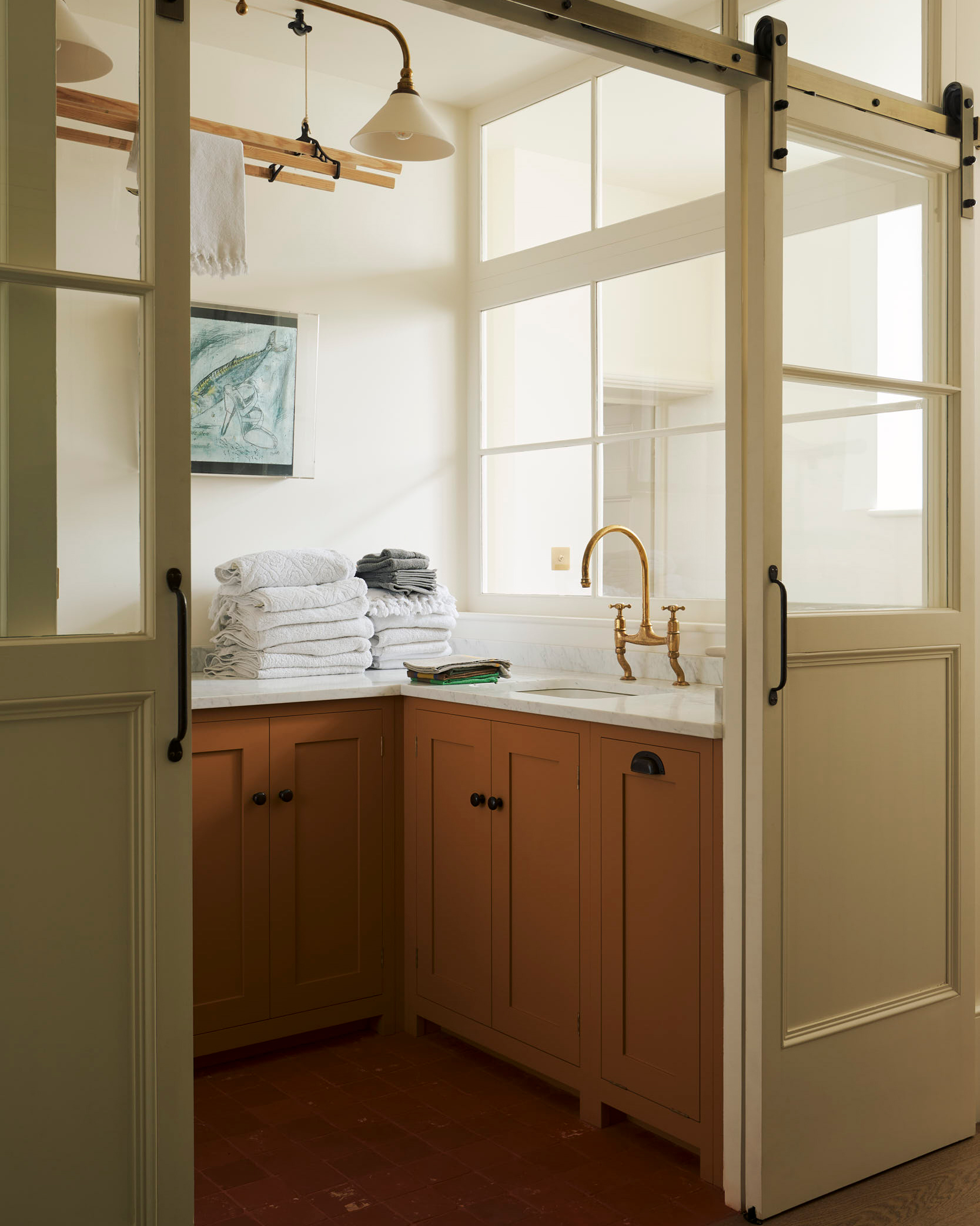 a laundry room inside white sliding doors, mustard cabinetry, white marble tops with towels folded on it, a wooden hanging clothes rail from the ceiling and a sink with gold tap