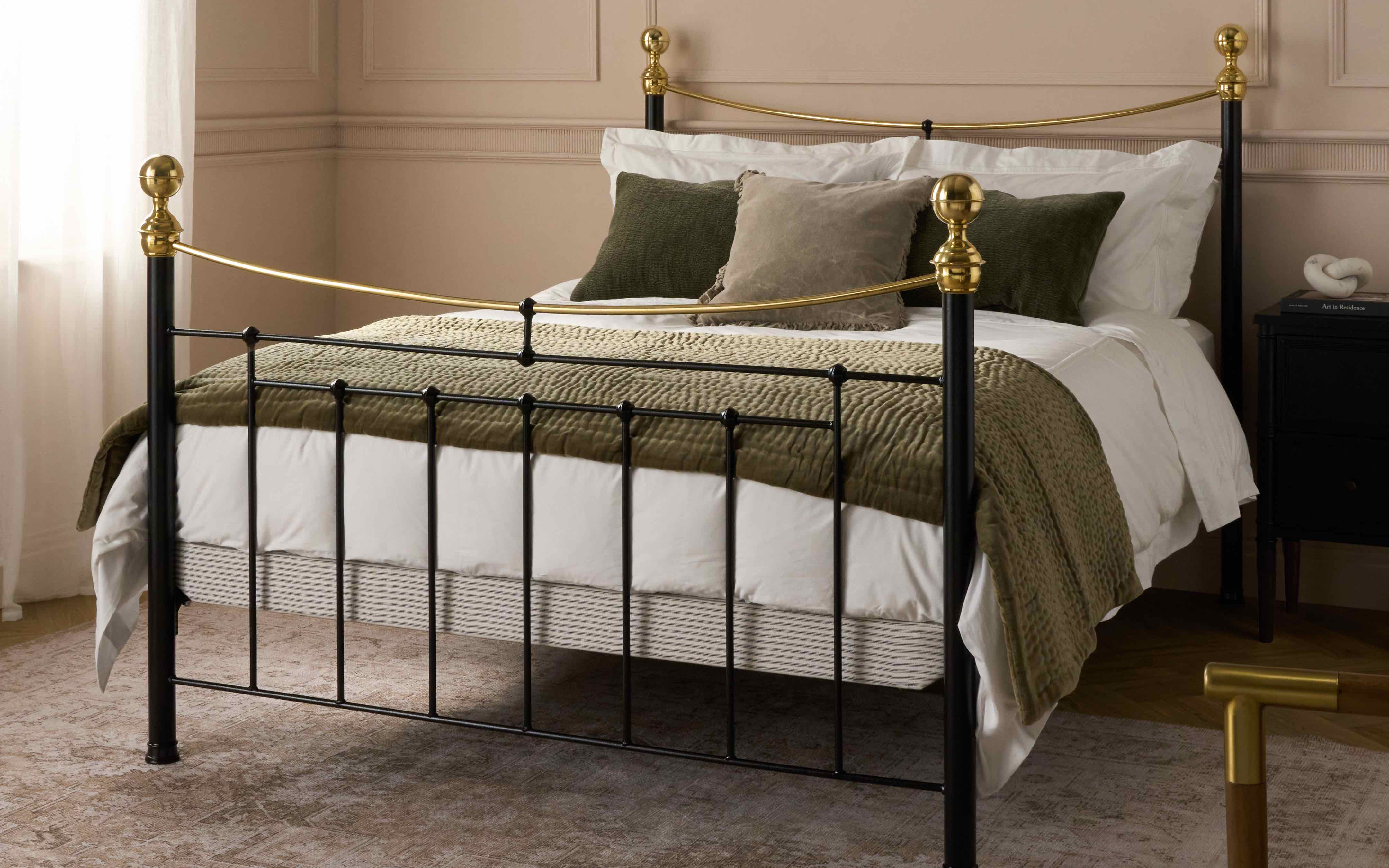 a black iron and brass bed frame with white bedding, olive green cushions and olive green throw