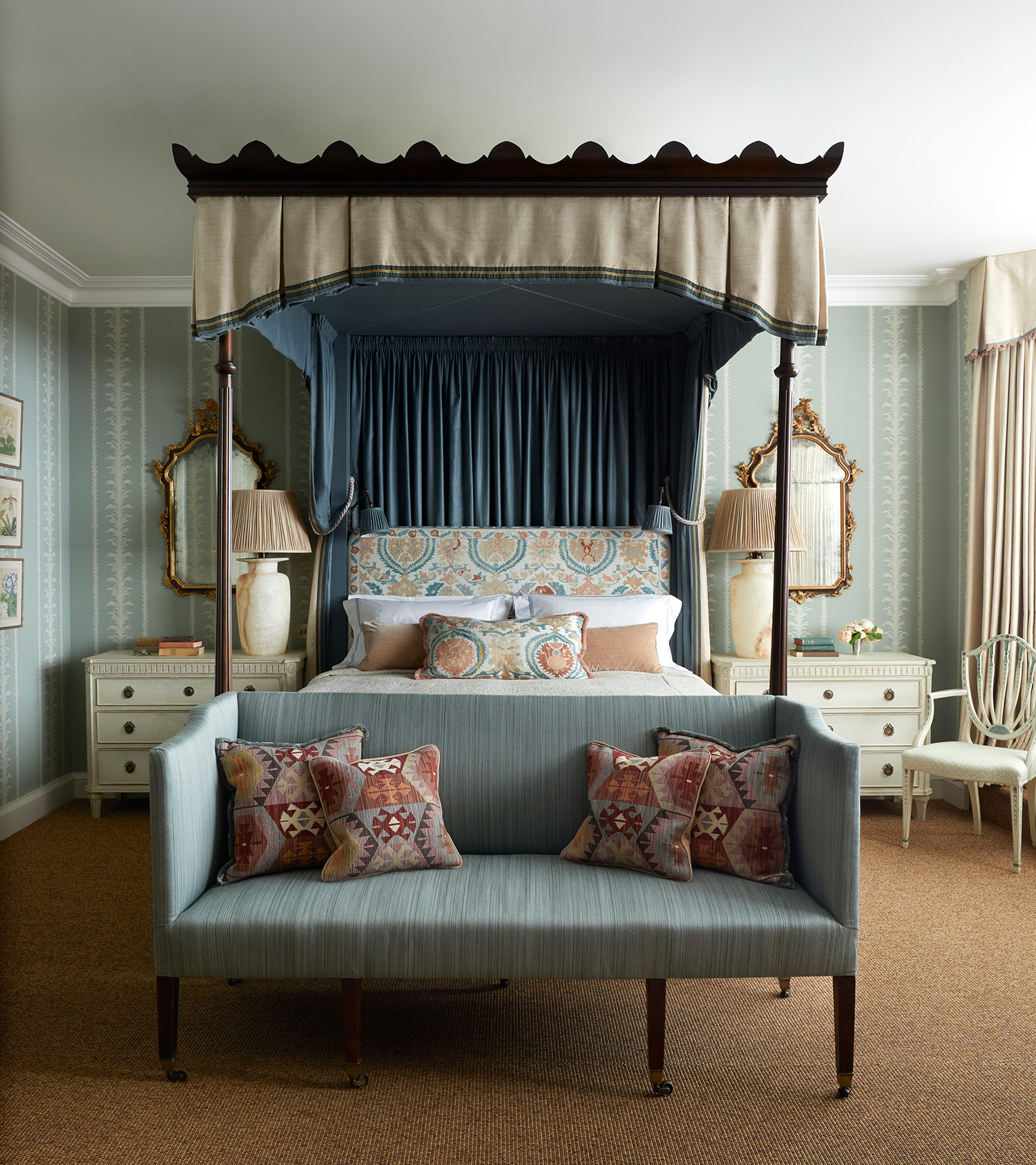 a traditional bedroom with a large four poster bed and a canopy, a patterned headboard, a blue sofa at the end of the bed, 