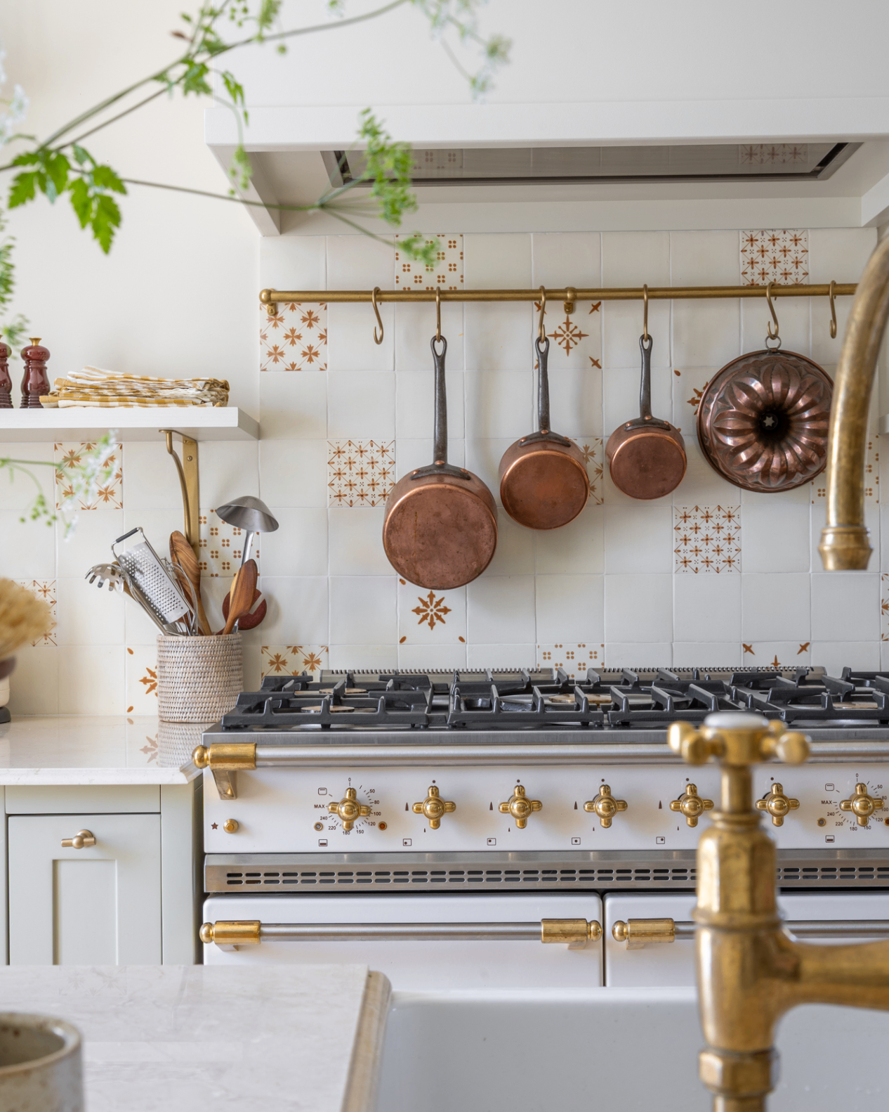 a kitchen with white and rust patterned tile splashback, a hanging rail with copper pans above a white range cooker