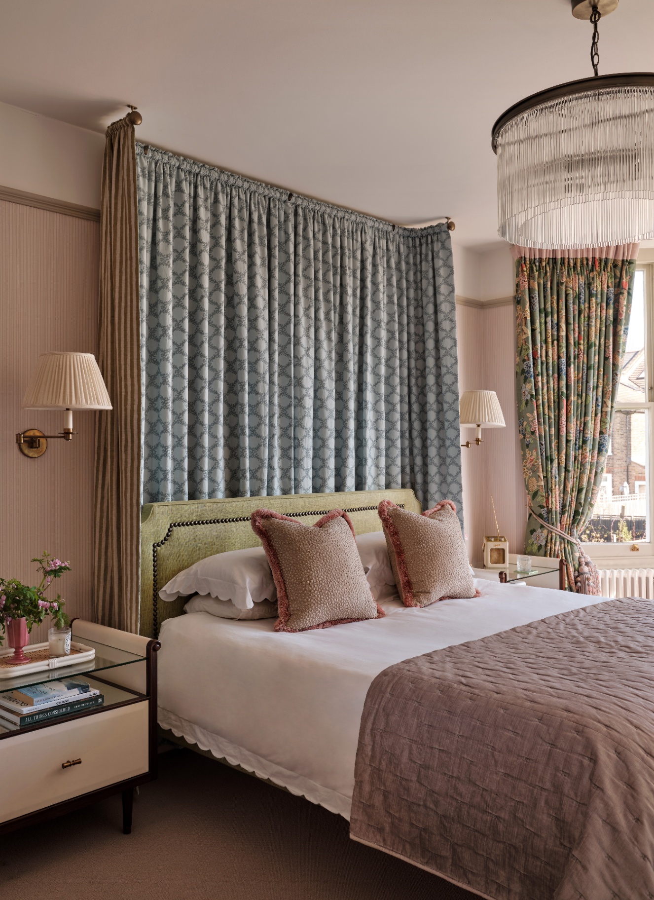  bedroom featuring a large round tiered fringe chandelier hanging centrally in front of a soft fabric backdrop and headboard drapery