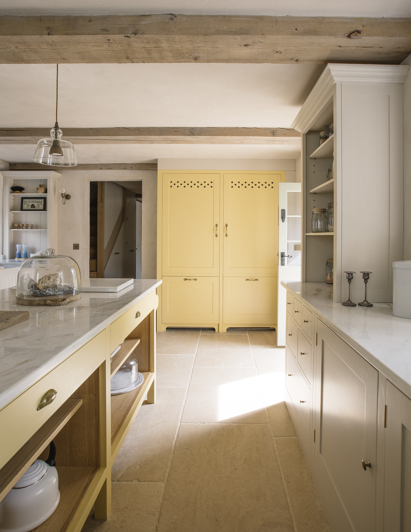a country kitchen with lemon yellow painted cabinets, wooden beams and a glass pendant shade