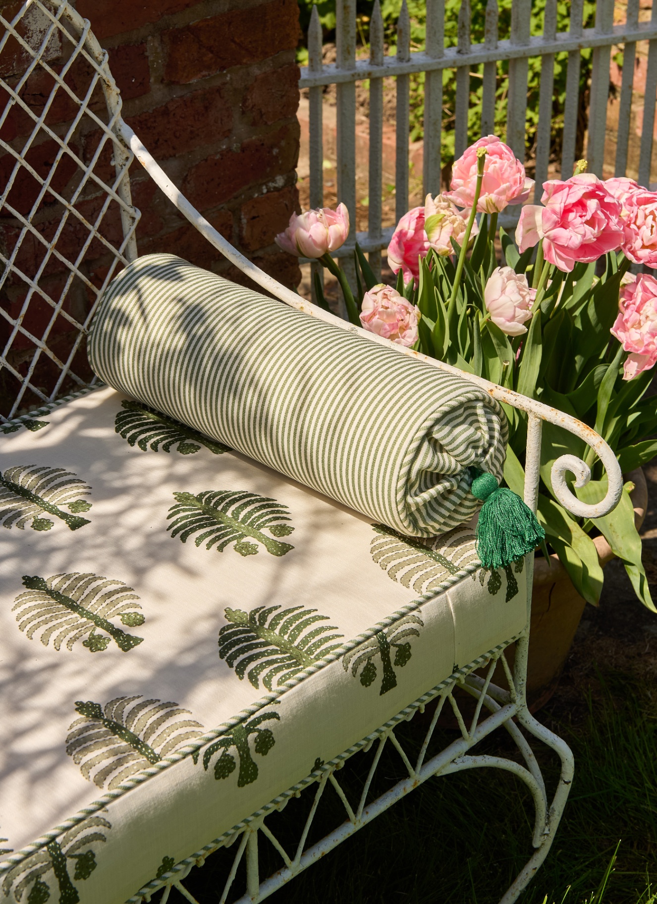 close up of a garden bench with white and green patterned cushions and pink flowers next to it