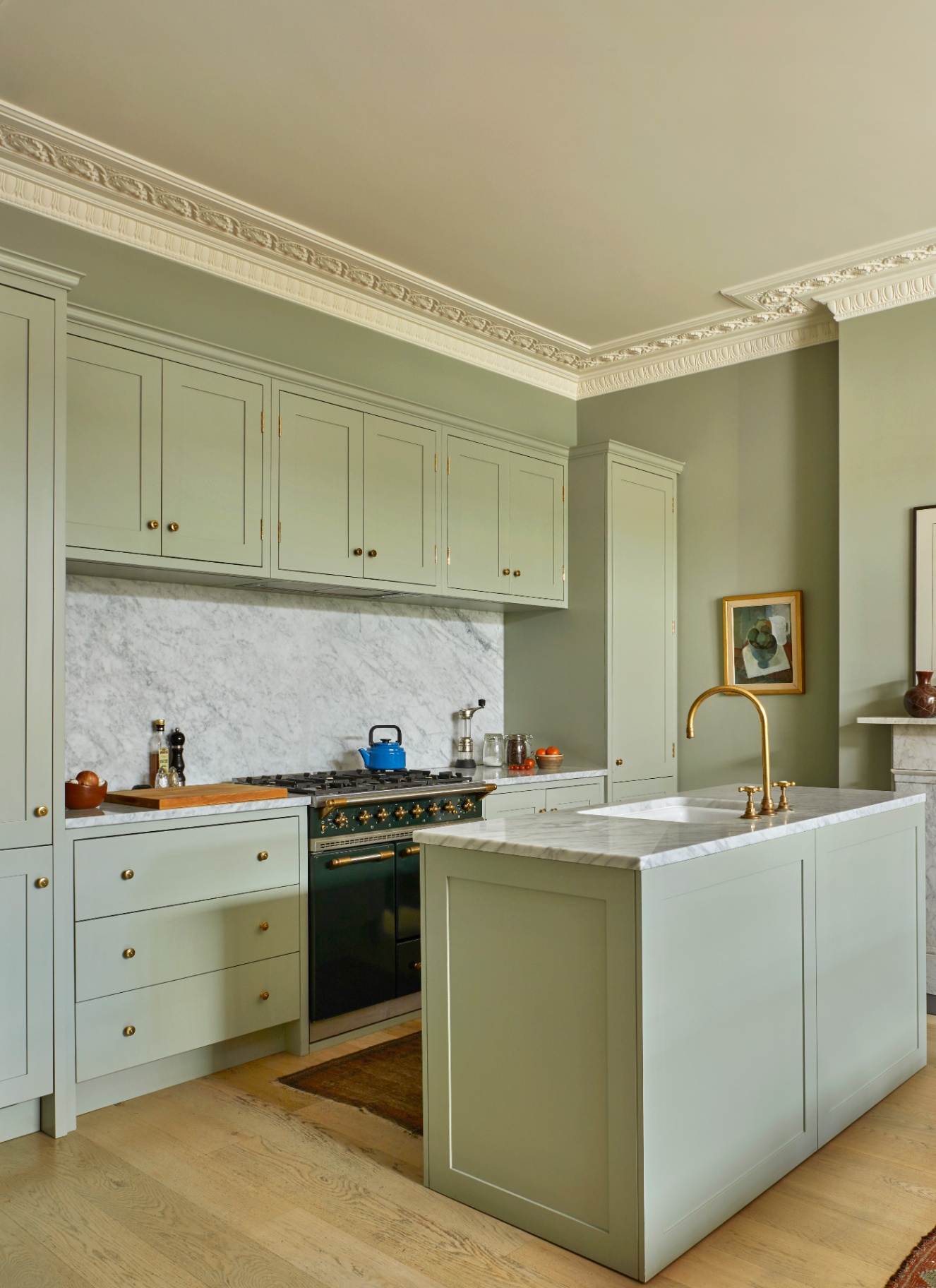 a small kitchen with pale green cabinetry, a pale green kitchen island, grey marble countertops and splashback and a dark green range cooker