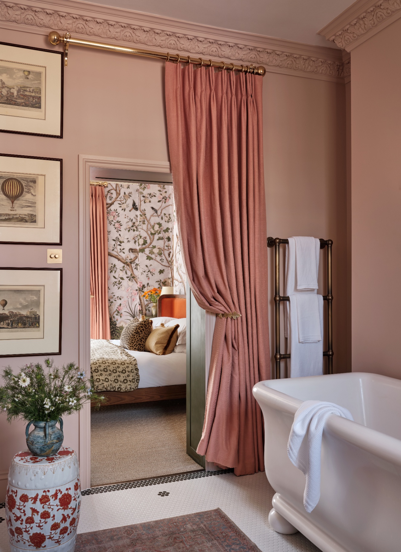 an ensuite bathroom with plaster pink walls, a freestanding bath, a pink curtained door looking out onto the bedroom and a heated towel rail with white towels