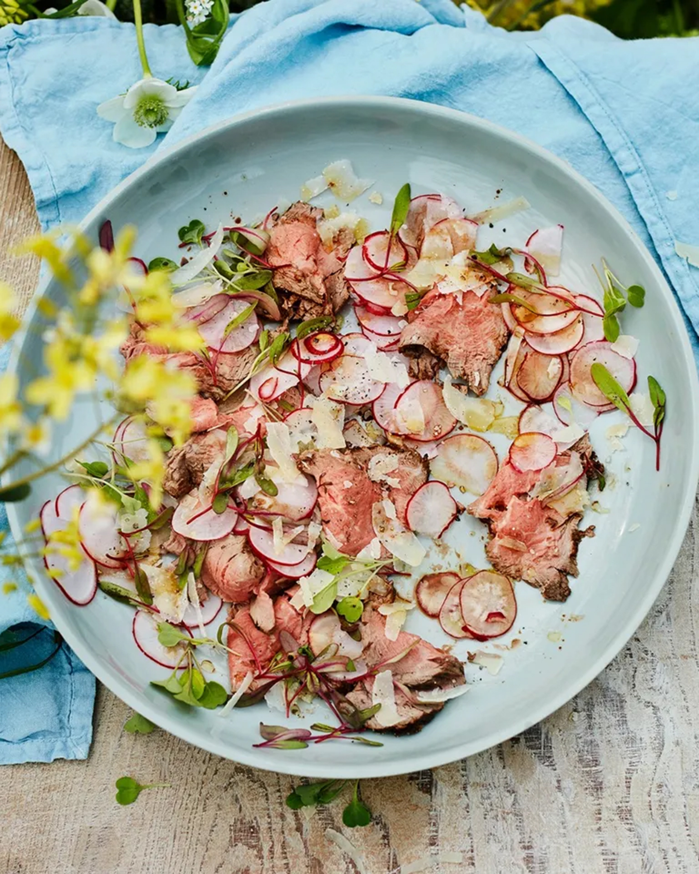 a white plate with a barbecue fillet of beef and radishes on a wooden table