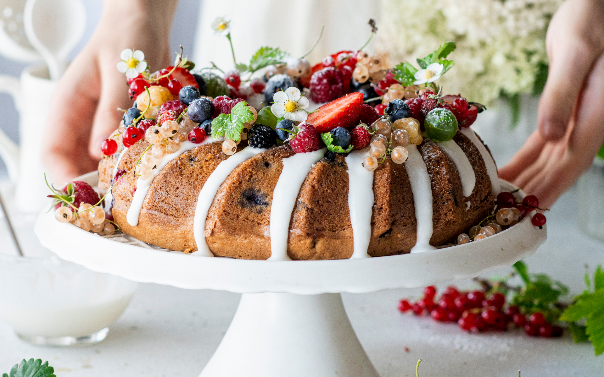 a wreath bundt cake topped with mixed summer berries on a white cake stand