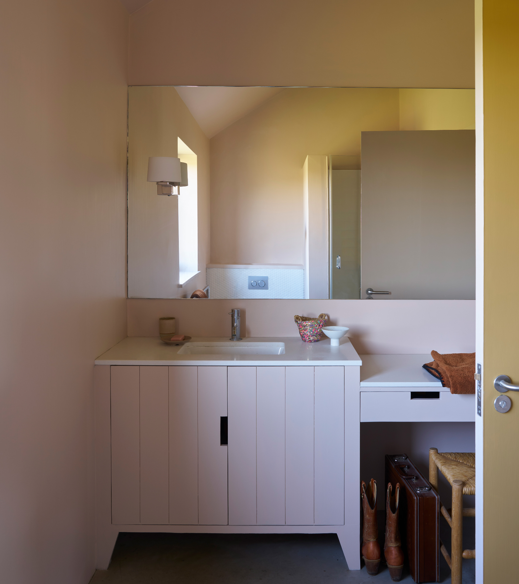 a downstairs toilet painted in a pale pink, with a large mirrored wall cabinet and a vanity and sink below it