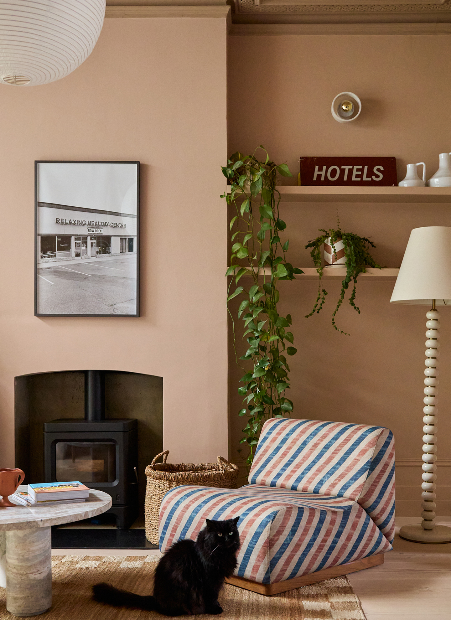 a living room with plaster pink walls, a large fireplace, a white, blue and pink striped chair and a black fluffy cat