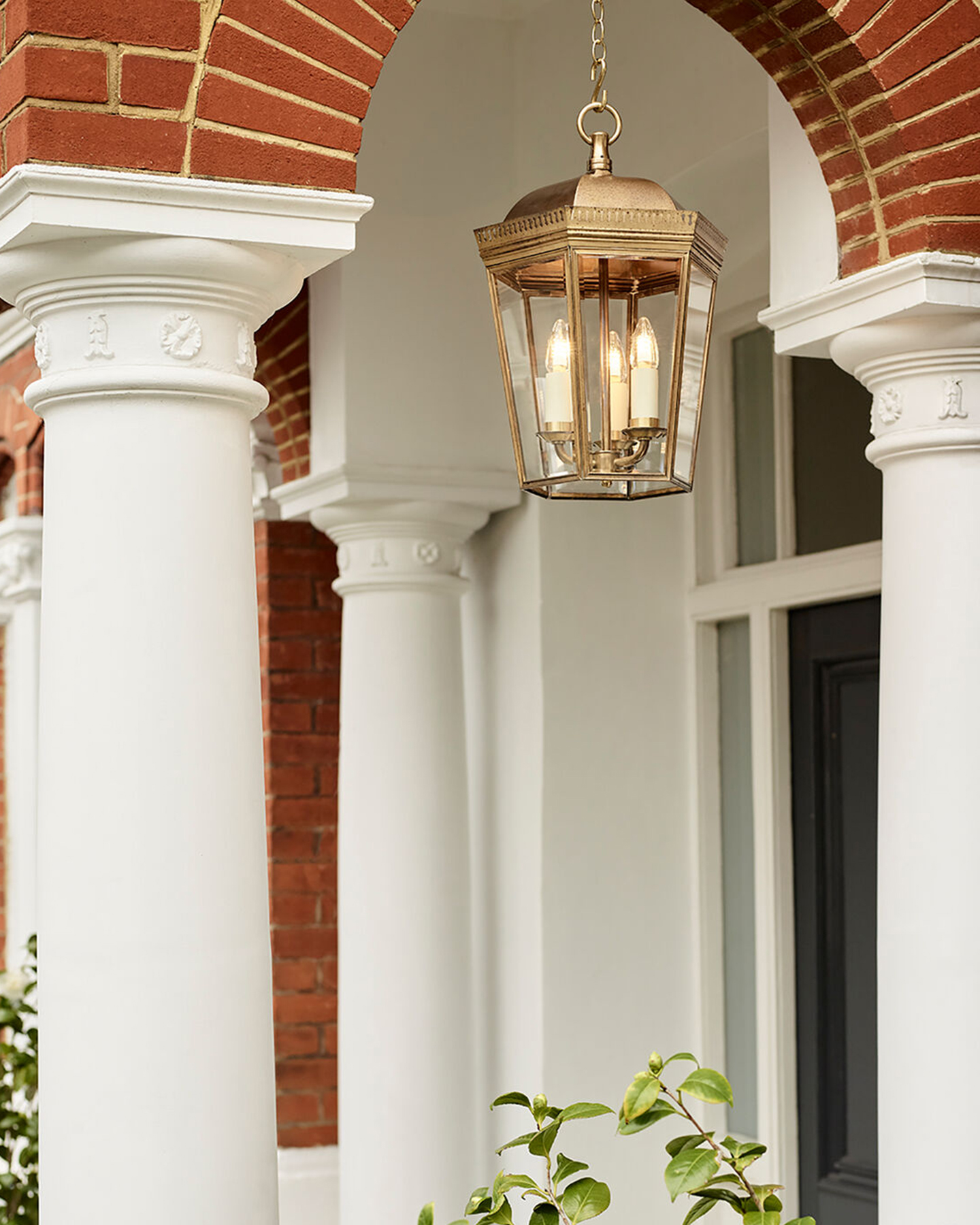 a front porch with white pillars, a large gold hanging pendent and a red brick arch