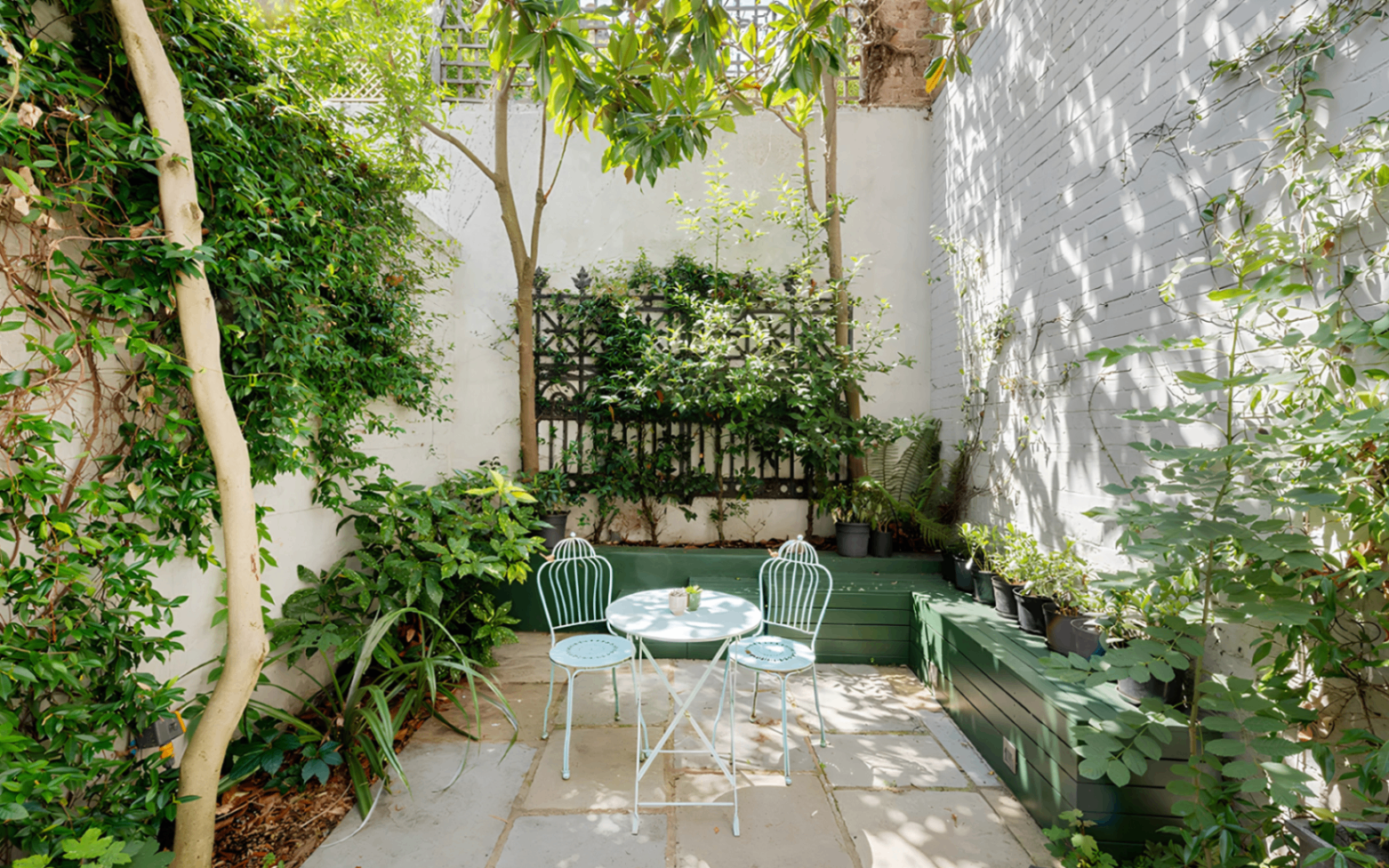 A garden terrace with a white bistro set and greenery