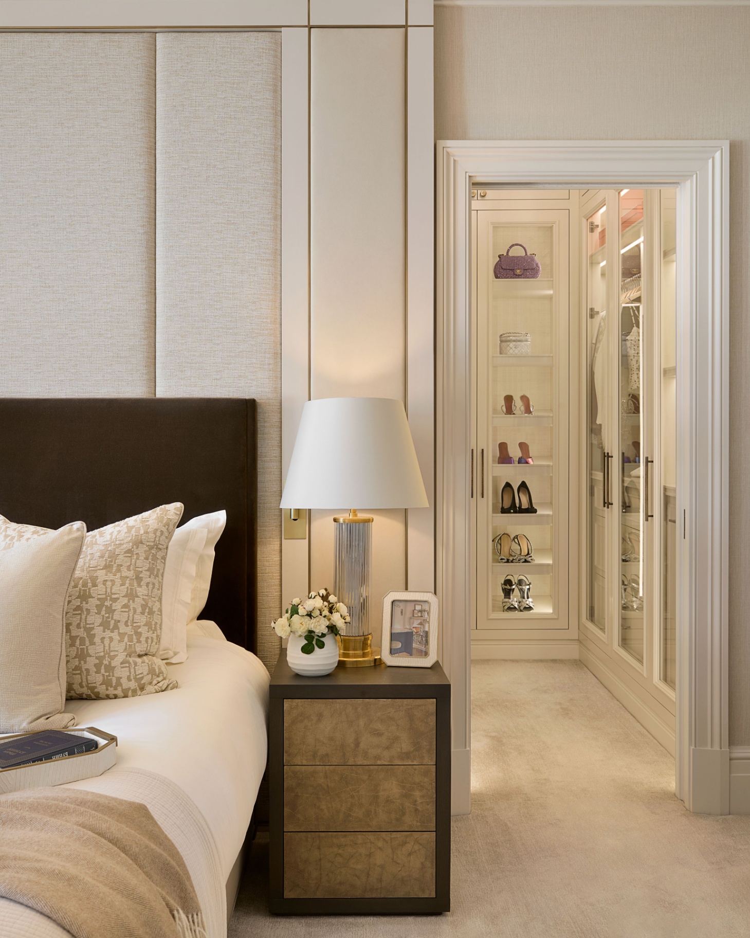 a neutral bedroom with an open door looking into a dressing room with open shelves full of shoes neatly lined up
