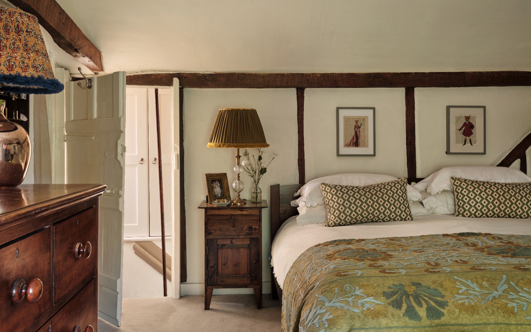 A rustic bedroom with exposed wooden beams, a patterned lamp, and a white door leading to a hallway