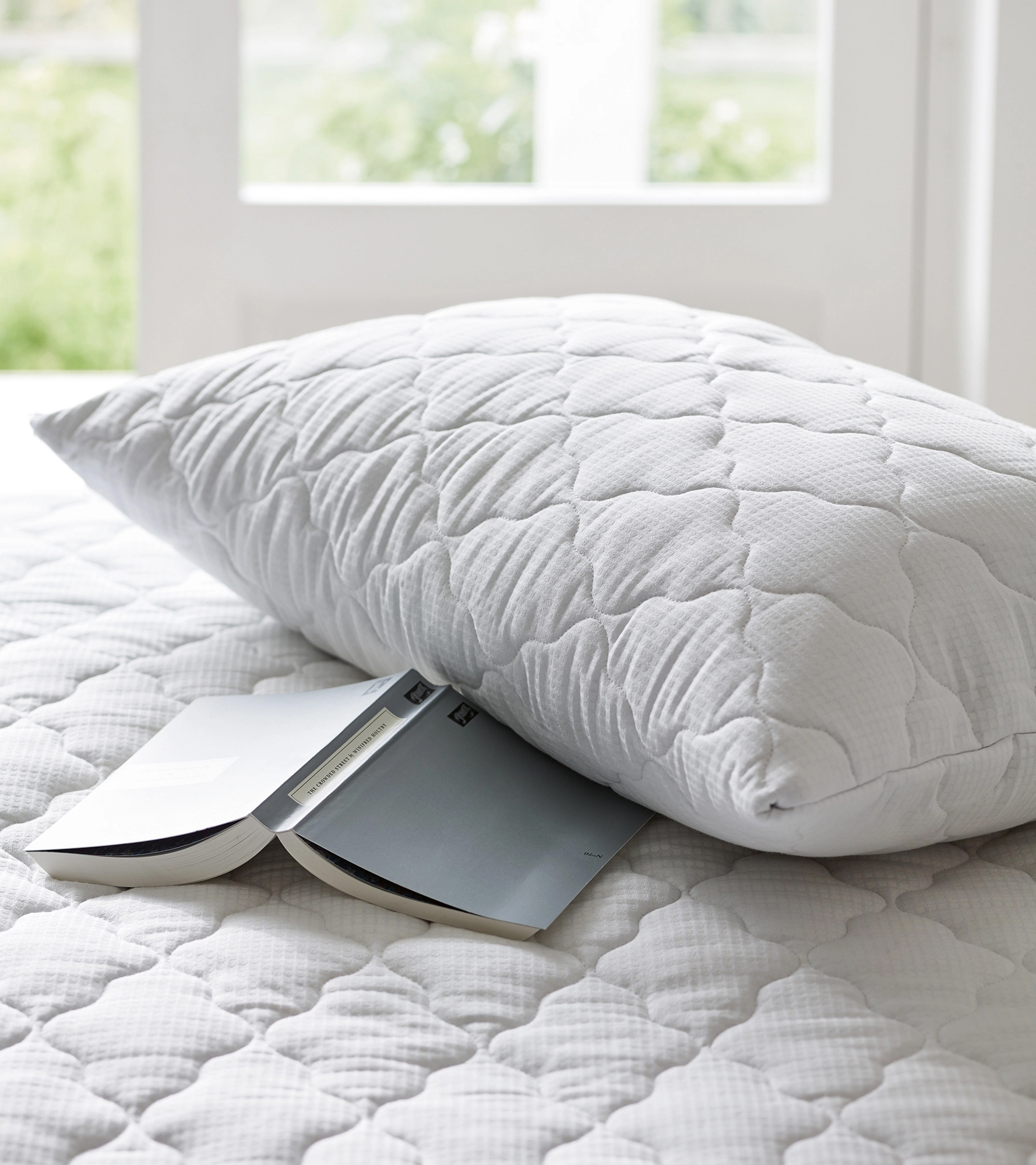 a pillow with a pillow protector on a mattress with an open book