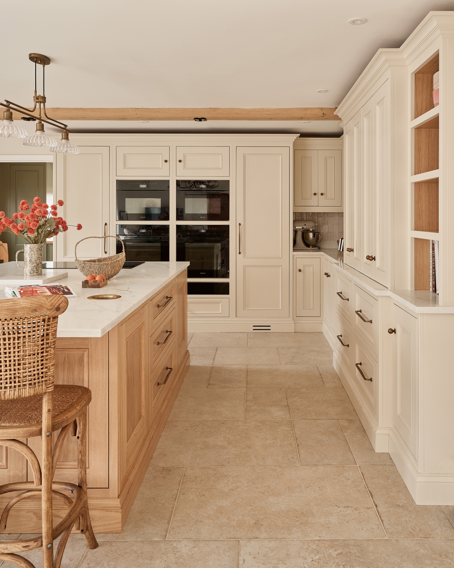 a kitchen with a stone floor, a light wooden kitchen island with a white marble top and a 3 light pendant hanging over the top of it
