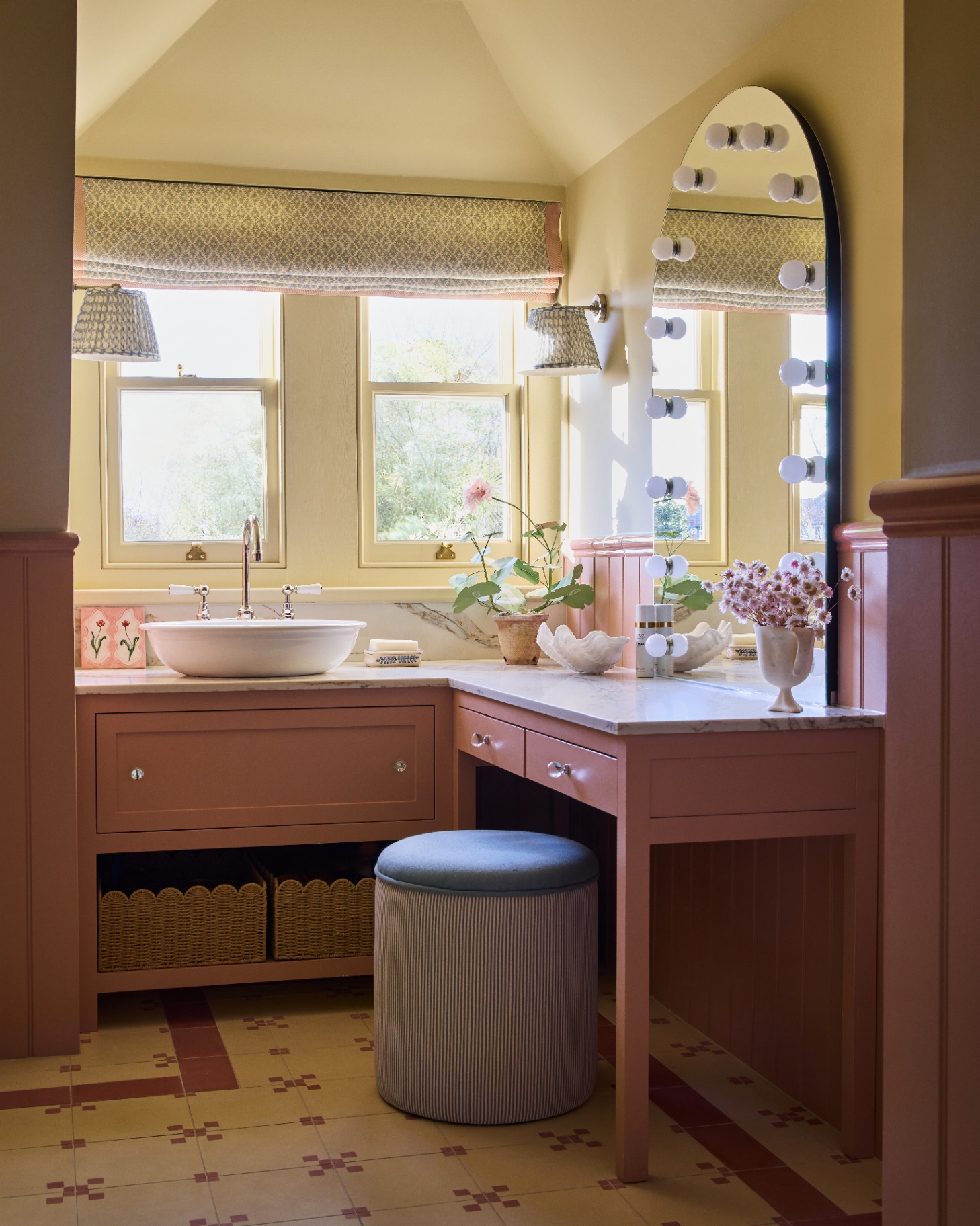 a quaint pink and yellow painted bathroom pictured with a vanity table and foot stool