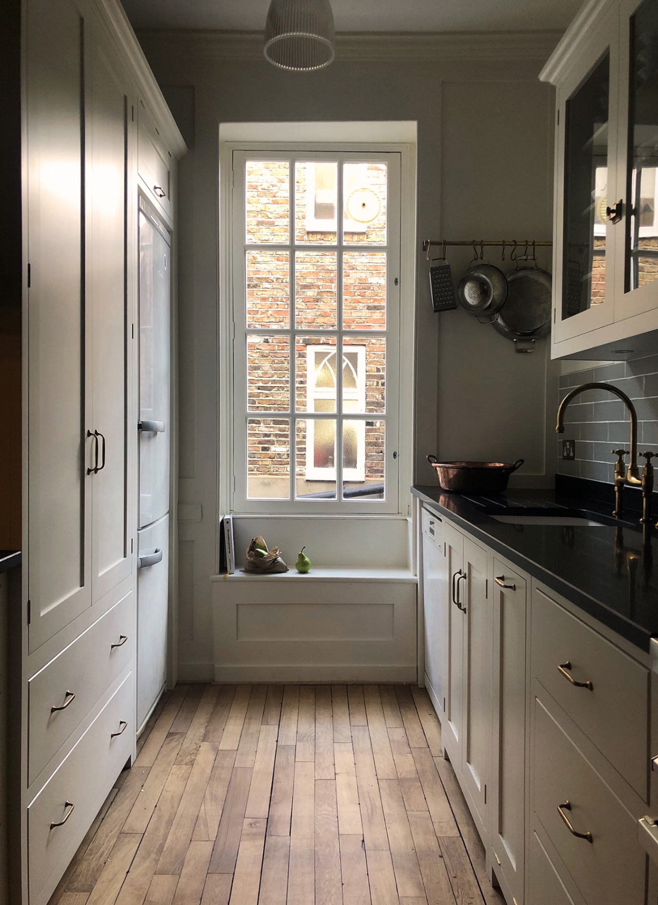 a narrow kitchen with greige cabinetry and a large sash window