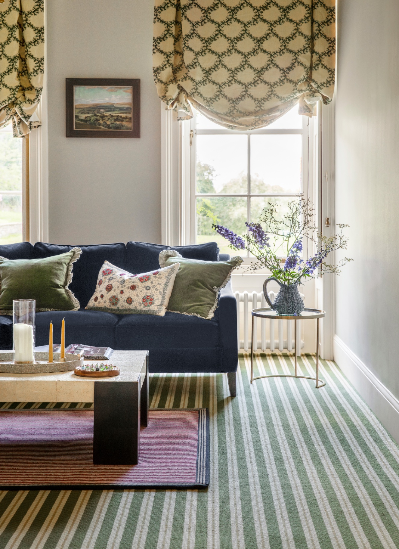 a living room with white walls, green and white striped carpets, a navy sofa and green and white patterned blinds