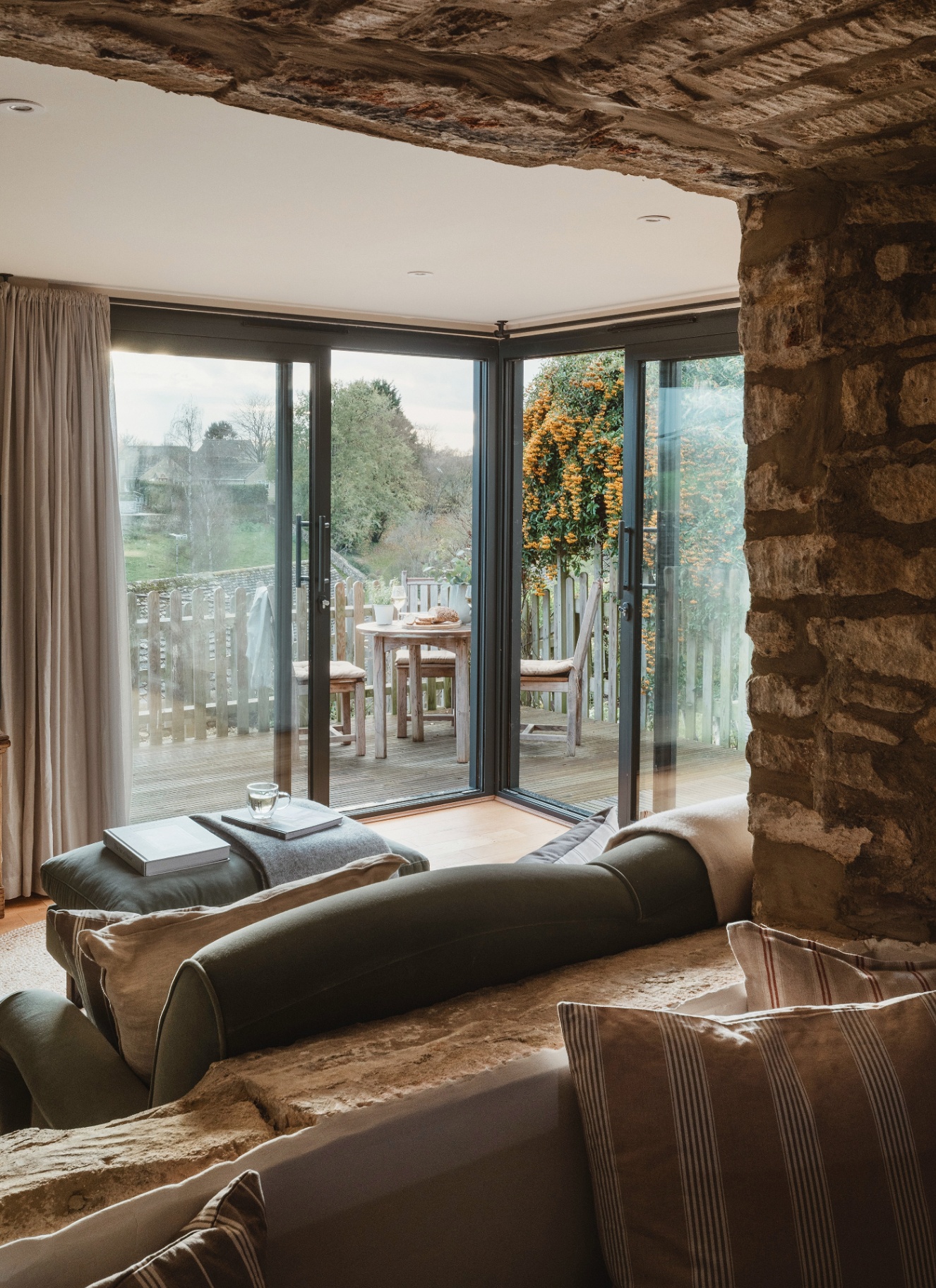 a living room with an exposed brick archway looking through to the room with sage green sofas looking out to the view outside