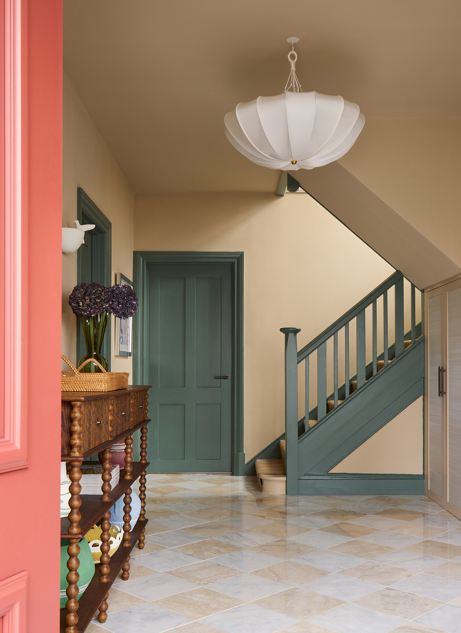 a hallway with beige and white checkerboard flooring, teal painted doors and stairs and a wooden bobbin console table