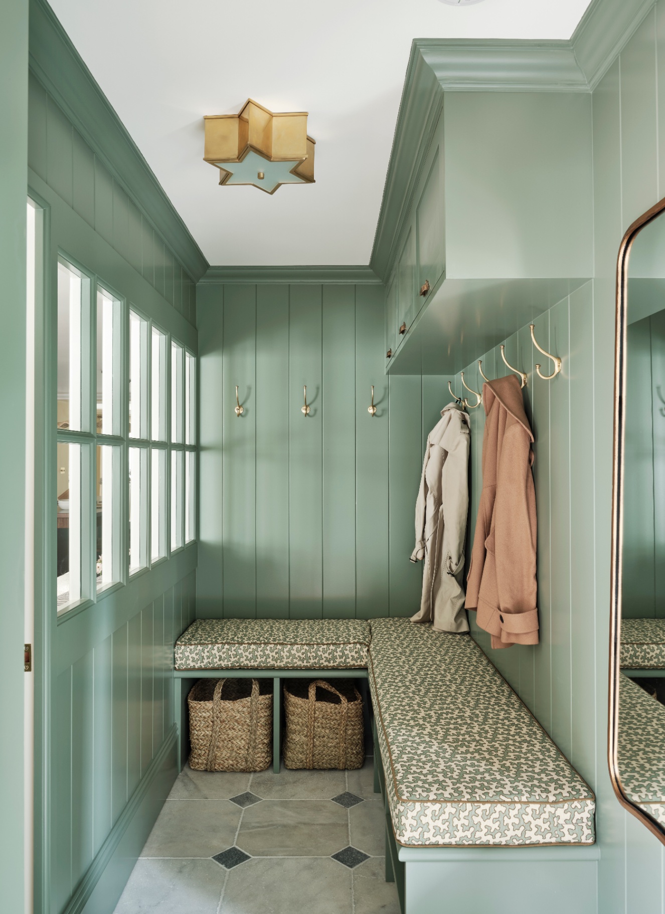 a narrow bootroom with mint green walls, a corner bench with a white and green patterned bench cushion and gold hooks with two coats hanging from them