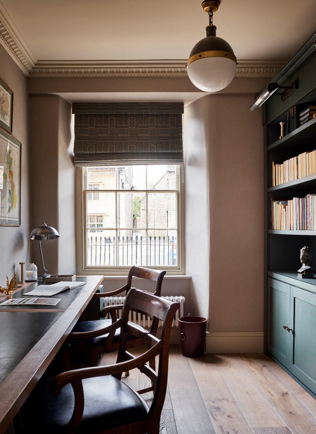 a home study office room with pale walls, a long wooden desk, two wooden chairs and a built in green bookcase