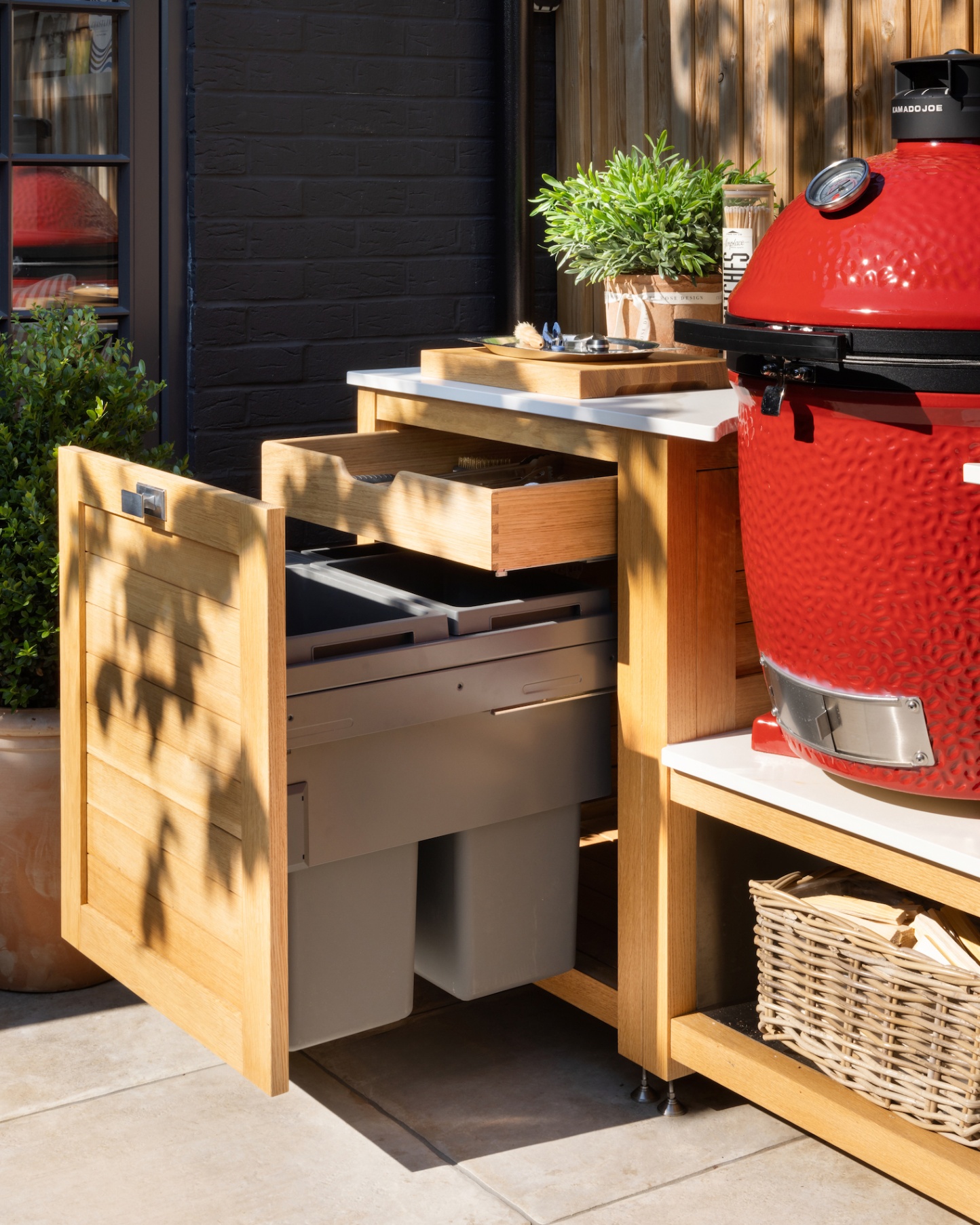 an outdoor kitchen with pull out built in bins and drawers and a large bright red bbq