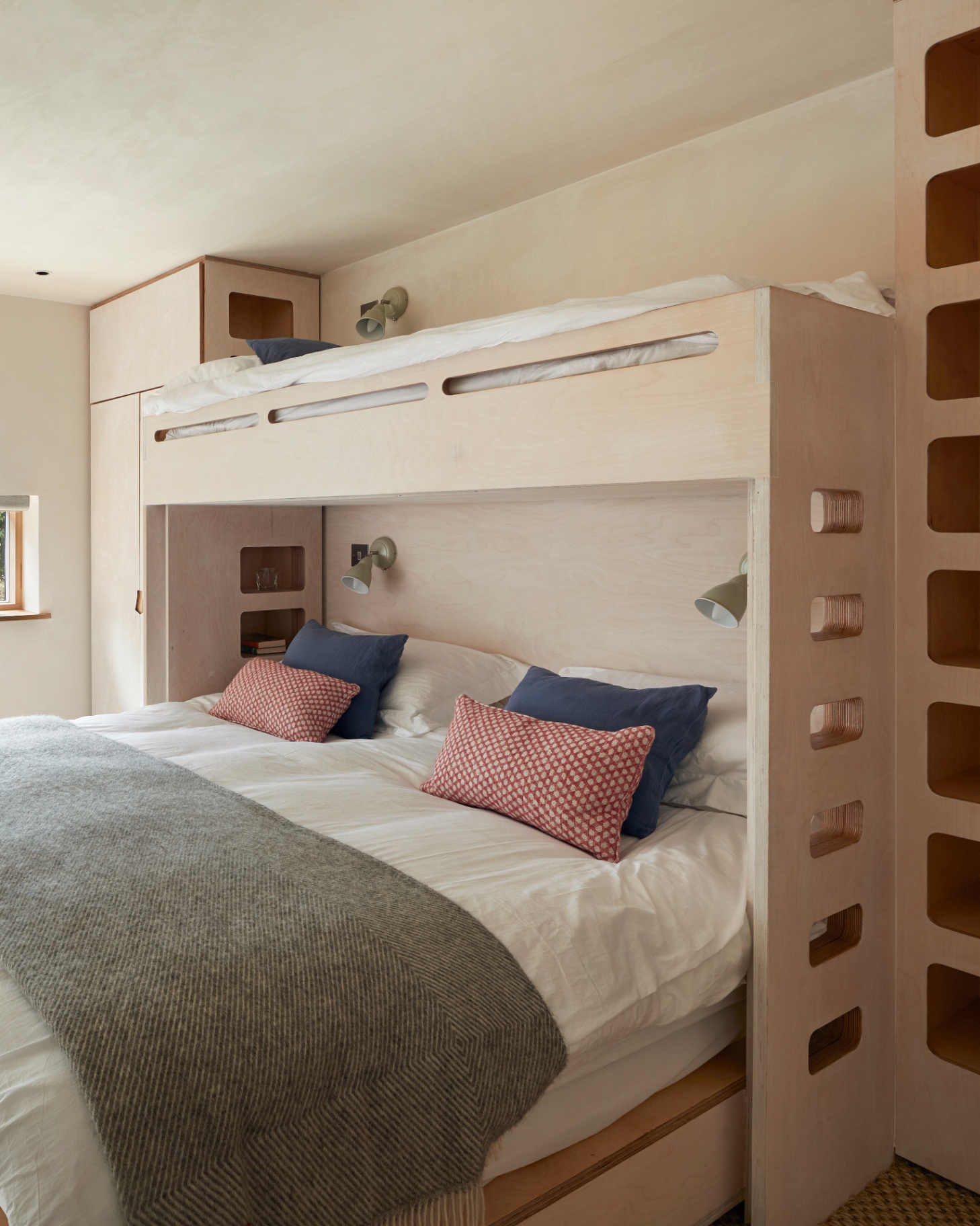 a bedroom with abuilt in bunk bed painted in cream and a bed underneath with white bedding and a green throw