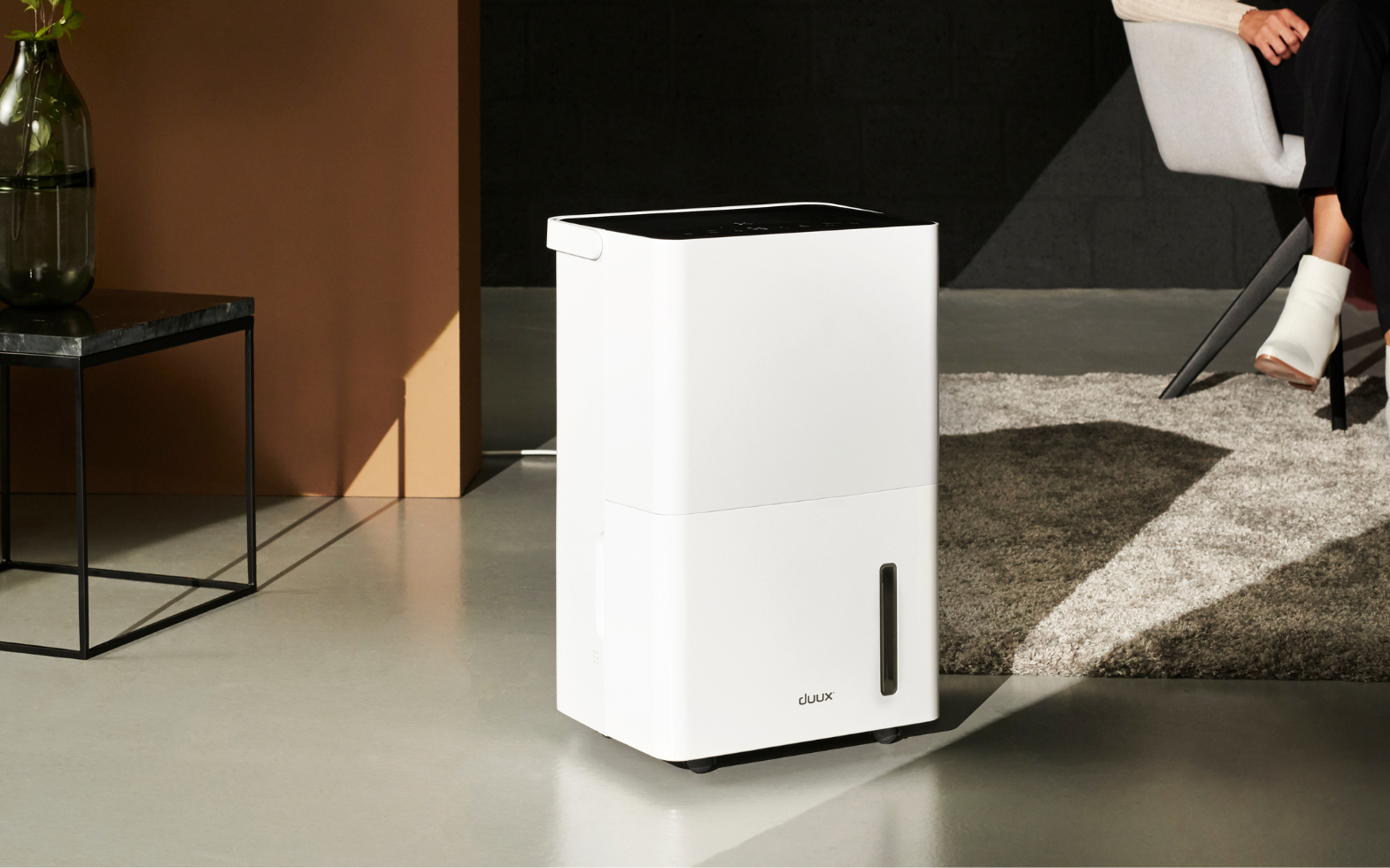 a white dehumidifier on a grey hard floor in front of a grey fluffy rug