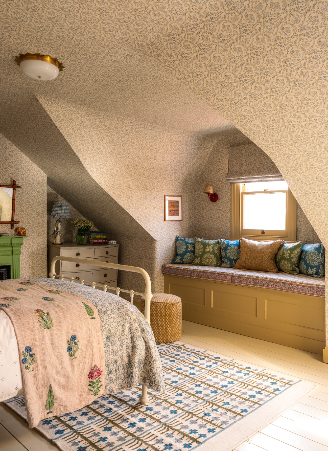 a bedroom with sloping ceilings with white and pale grey botanical wallpaper on the walls and ceilings, a white iron bed and a window seat with cushions