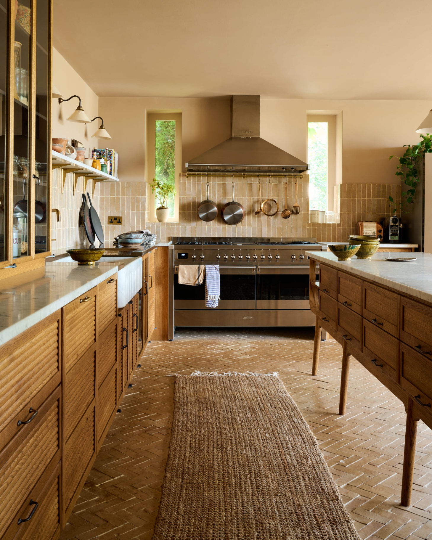 a kitchen with herringbone brick floor, a jute runner, wooden cabinetry and wooden island with marble tops and a large silver cooker