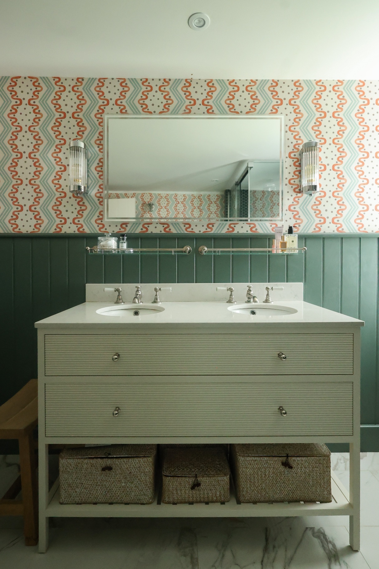 a bathroom vanity pictured in sage green in front of wallpaper walls and a rectangle mirror hangs above