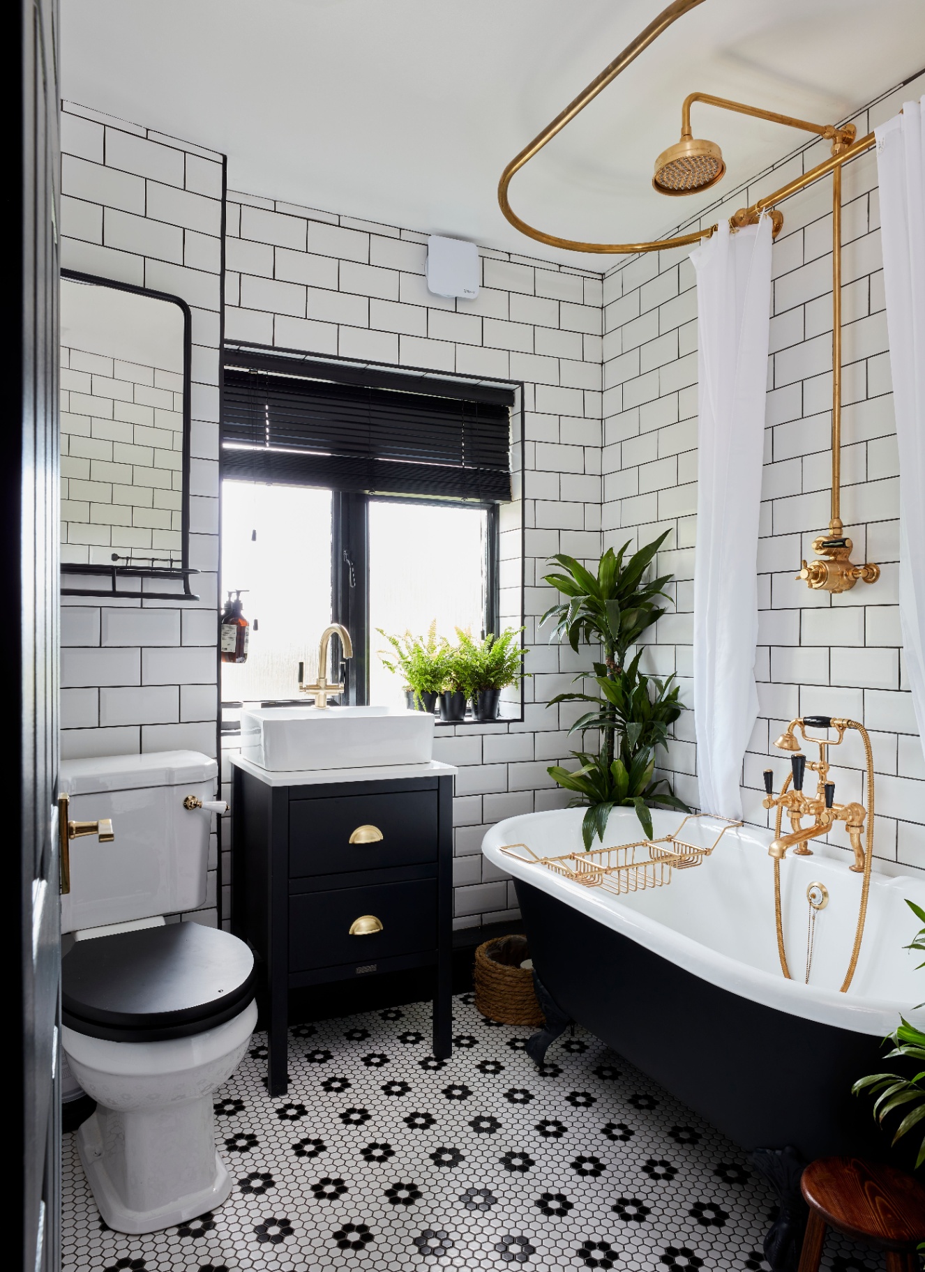 a bathroom with a black freestanding bath, a white and black floor tiles and gold hardware