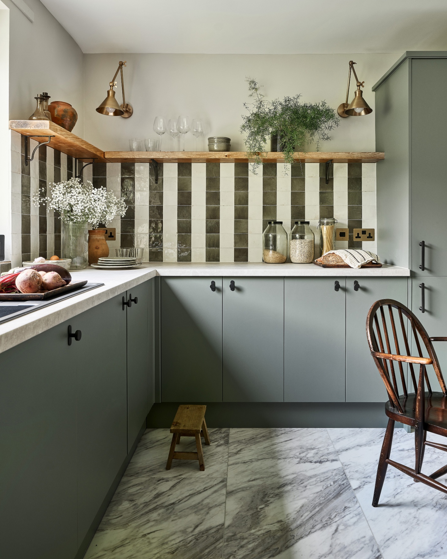 a kitchen with white and olive green tiled splashback laid out in a stripe pattern, white and grey marbled flooring and grey kitchen cabinets with black handles